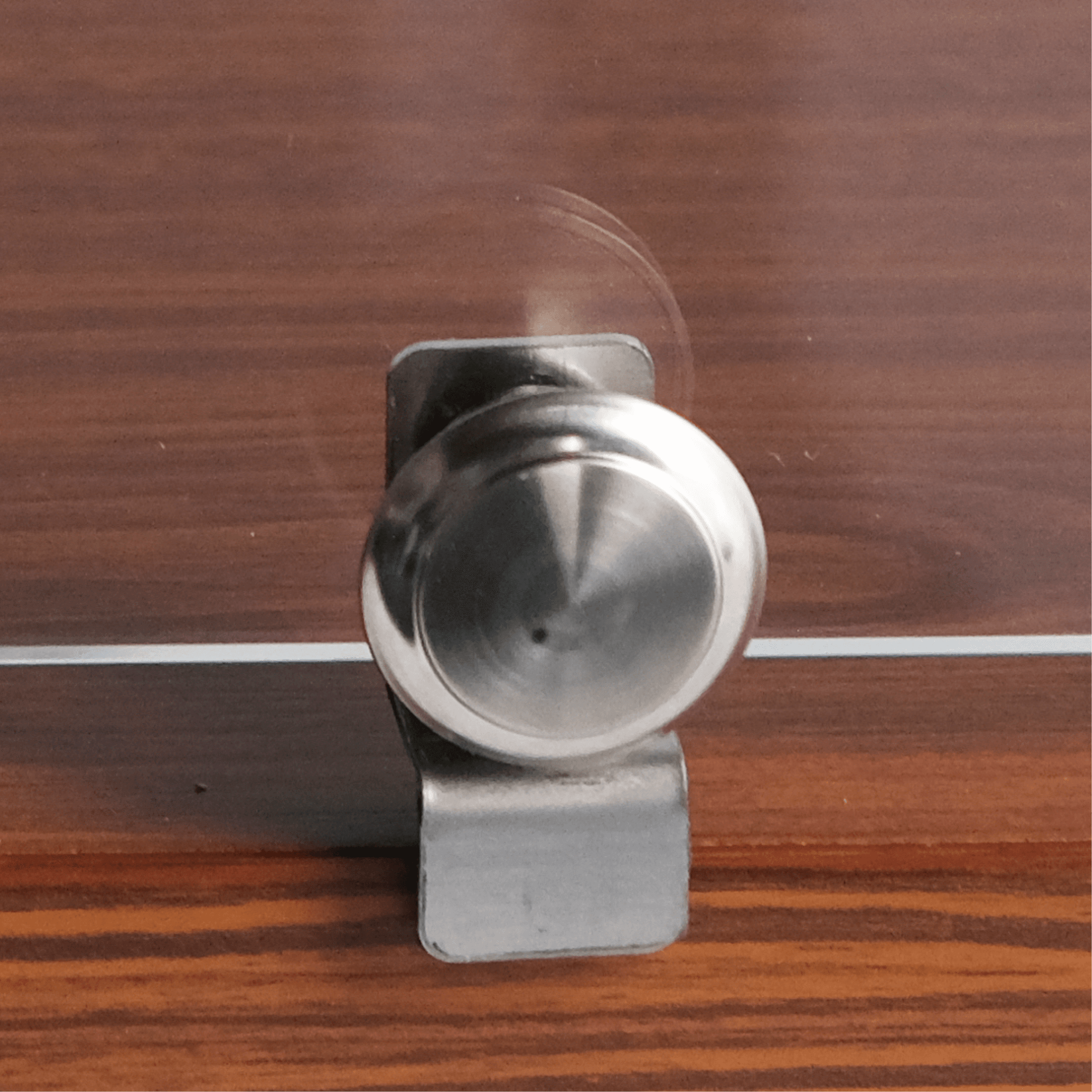 Close-up of round silver metal latch on walnut wood surface with subtle grain texture.