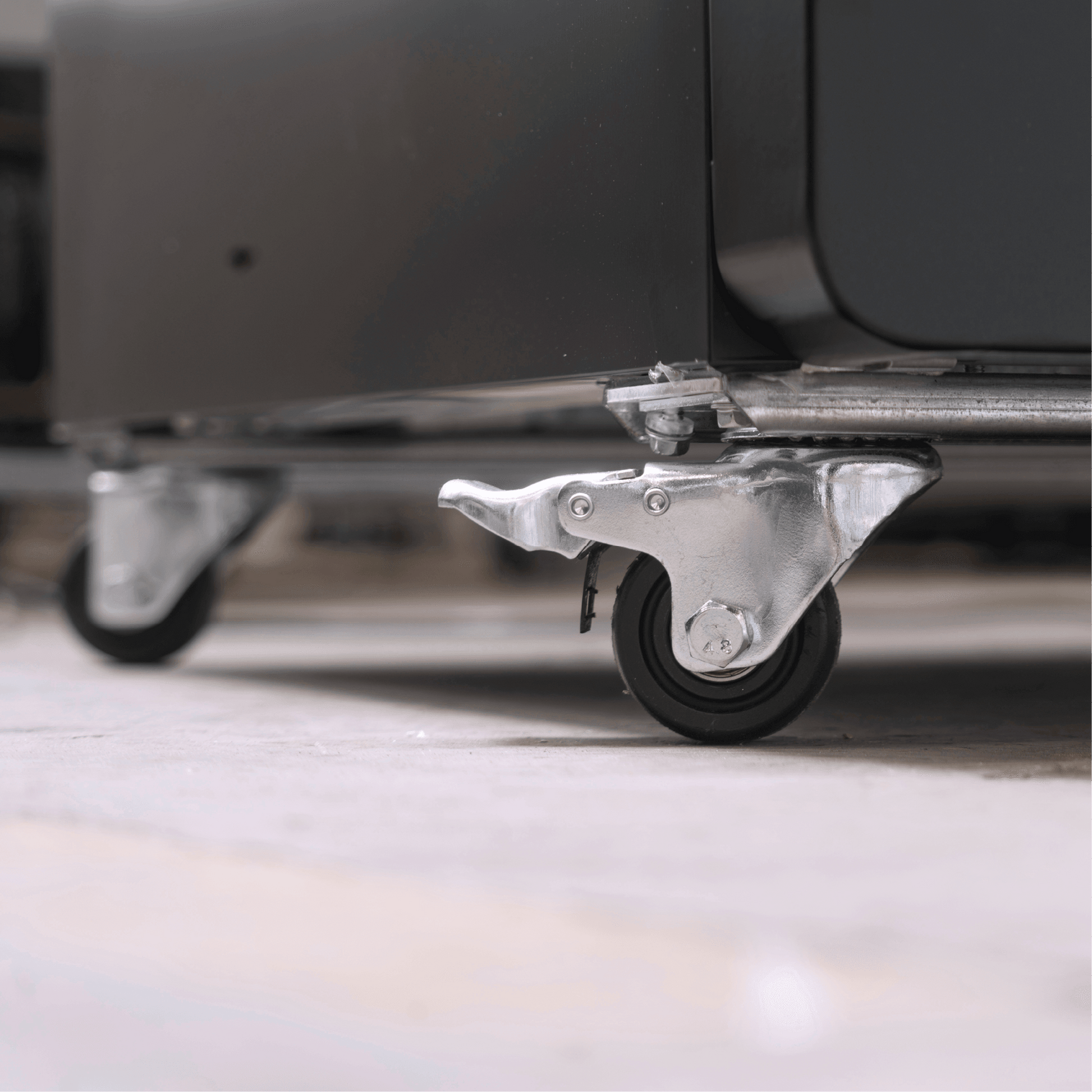 Close-up of black upright display refrigerator with metal caster wheel on light floor.