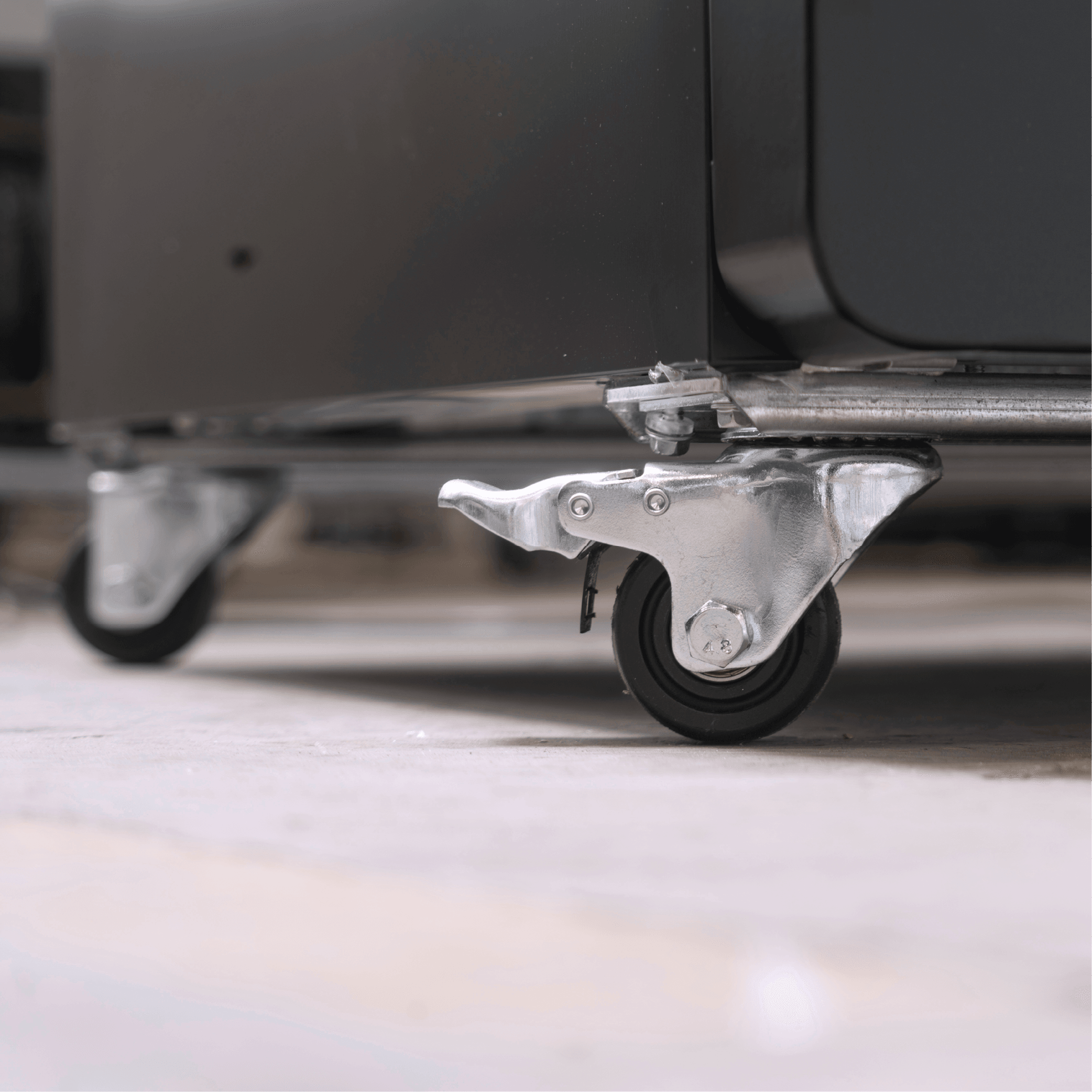 Close-up of black upright display refrigerator with metal caster wheel on light floor.