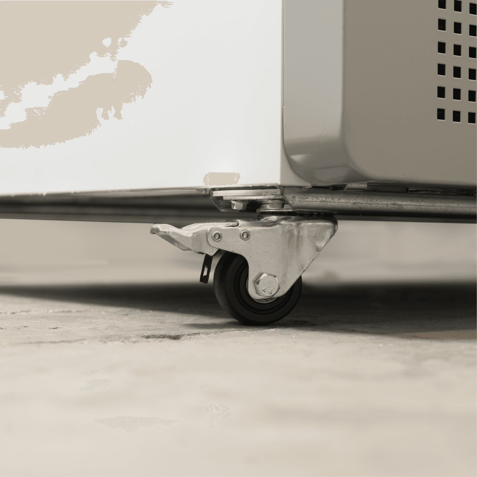 Close-up of metal caster wheel with brake attached to white painted steel base of upright display refrigerator.