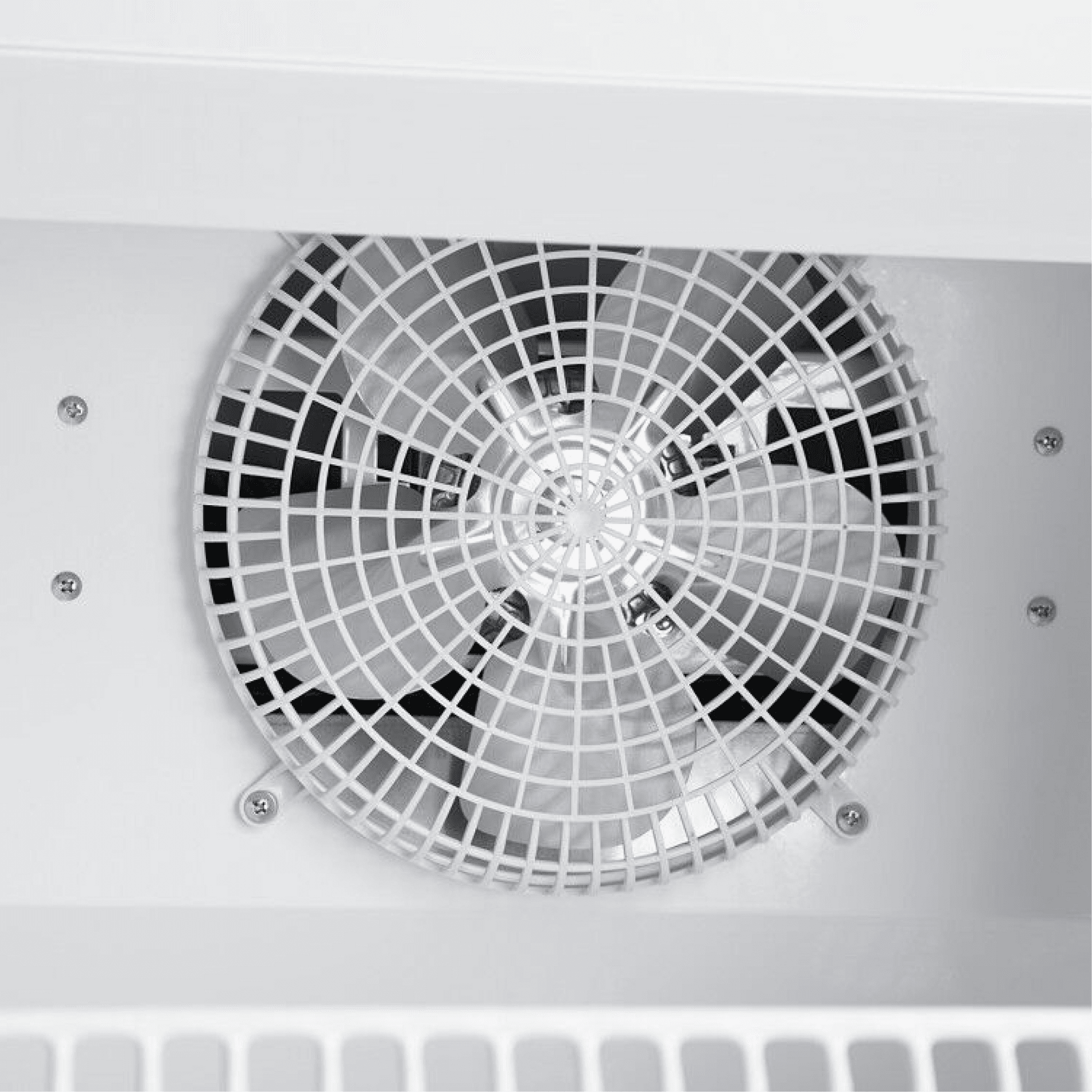 Close-up of circular metal ventilation fan with white protective grille inside white painted steel refrigerator interior.