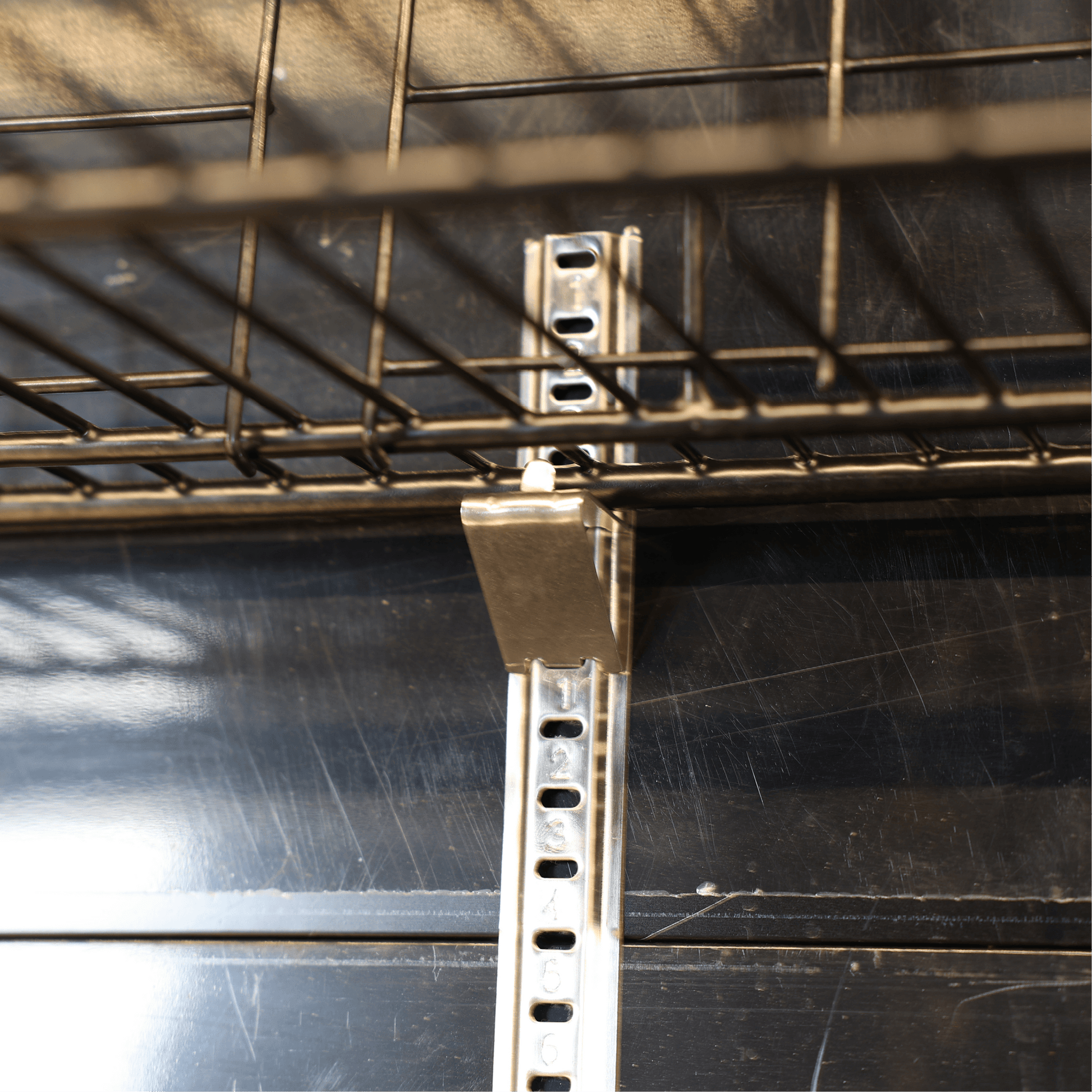 Metal shelving bracket and wire rack against black interior panel in upright display refrigerator.