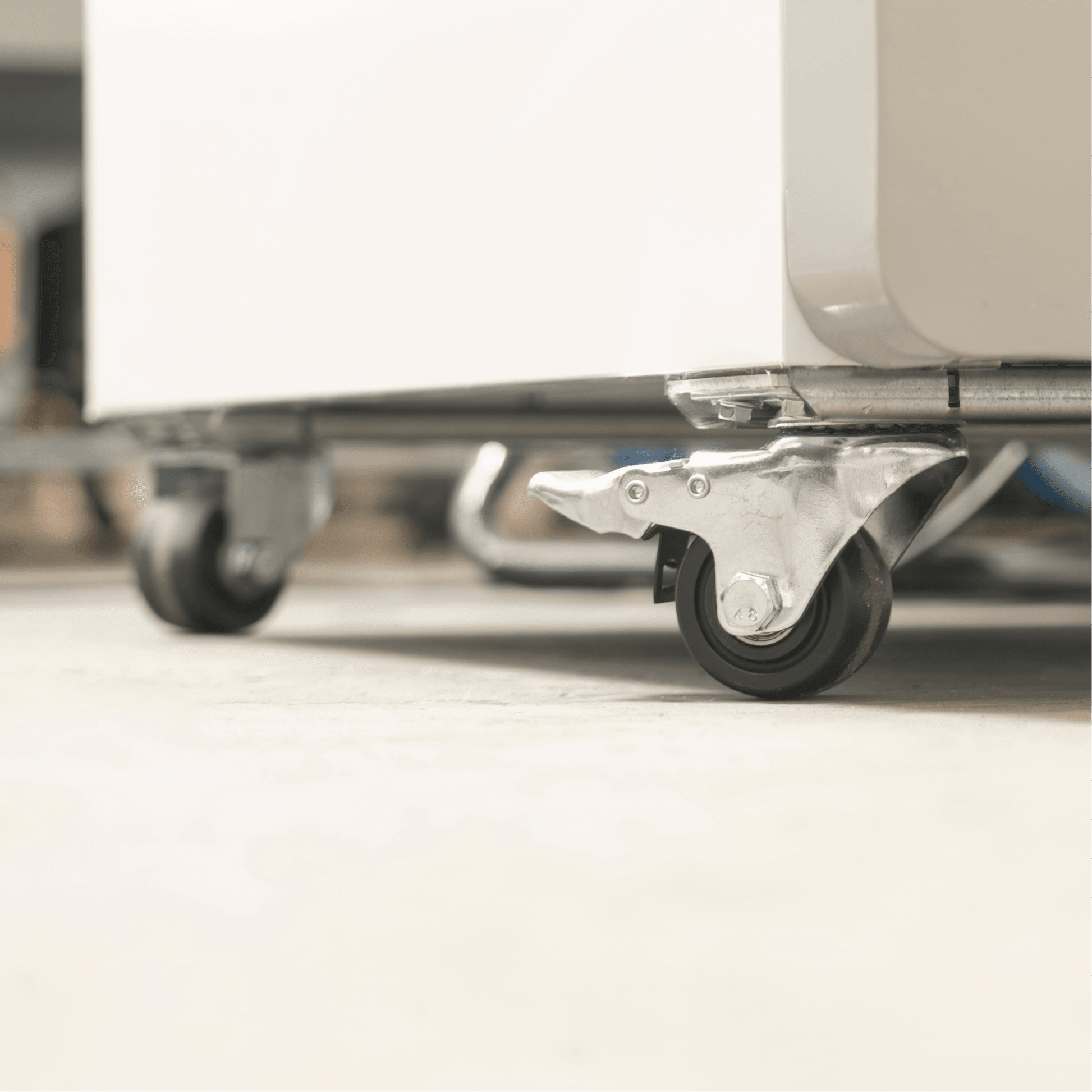 Close-up of a swivel caster wheel with metal bracket on white painted steel base of an upright glass door display fridge.