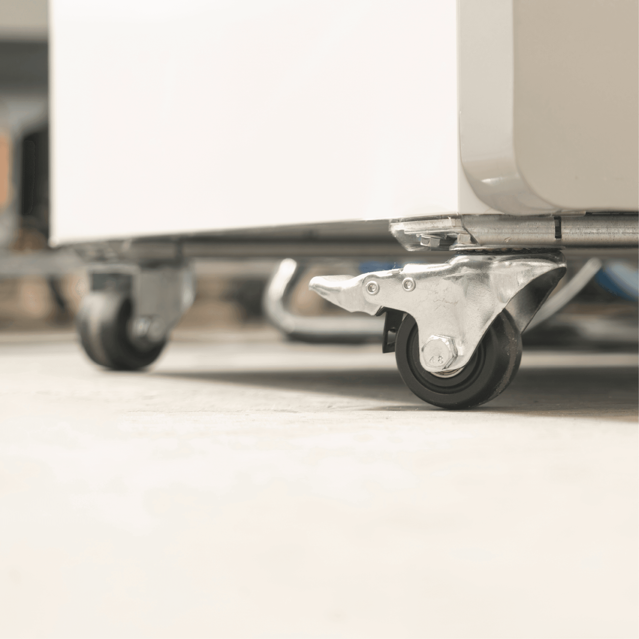 Close-up of a swivel caster wheel with metal bracket on white painted steel base of an upright glass door display fridge.