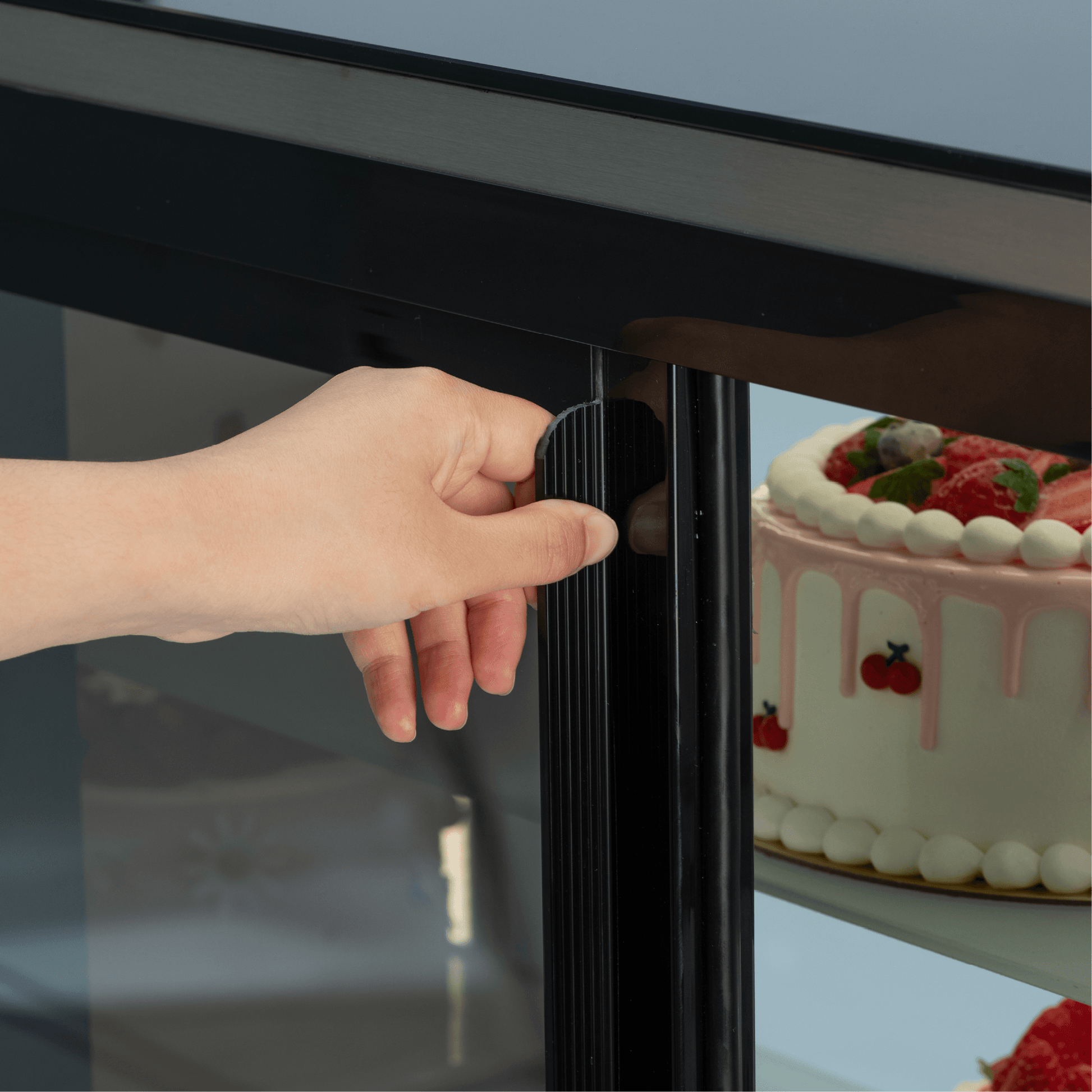 Black stainless steel cake display refrigerator door handle with glass panel and visible decorated cake inside.