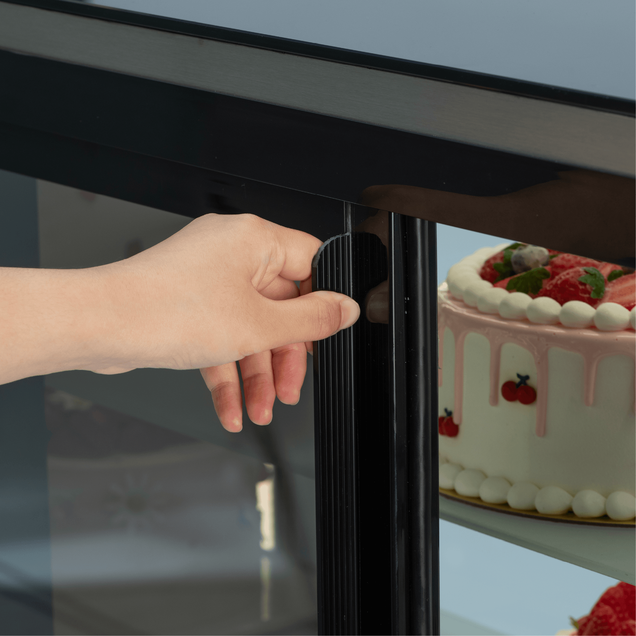 Black stainless steel cake display refrigerator door handle with glass panel and visible decorated cake inside.