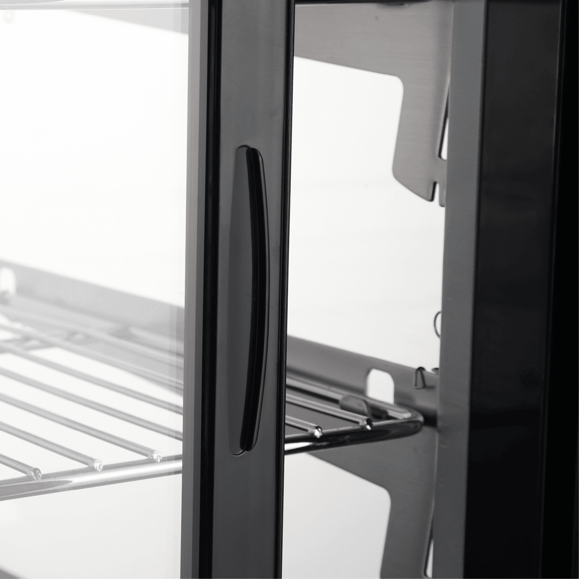 Curved stainless steel and glass cake display refrigerator door with black handle and metal shelving inside.