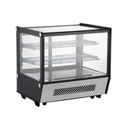 Compact stainless steel and glass counter top cake display refrigerator with three wire shelves and front ventilation panel.