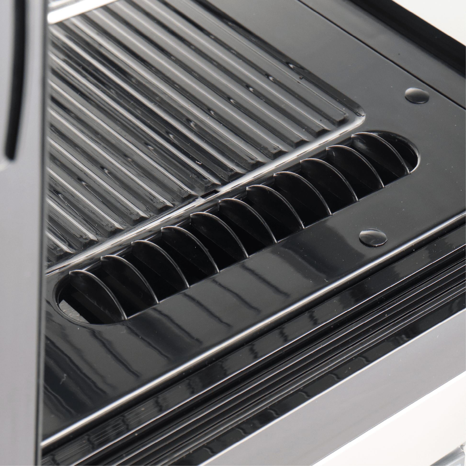 Close-up of black stainless steel interior with slotted ventilation and grooved shelving of curved cake display fridge.