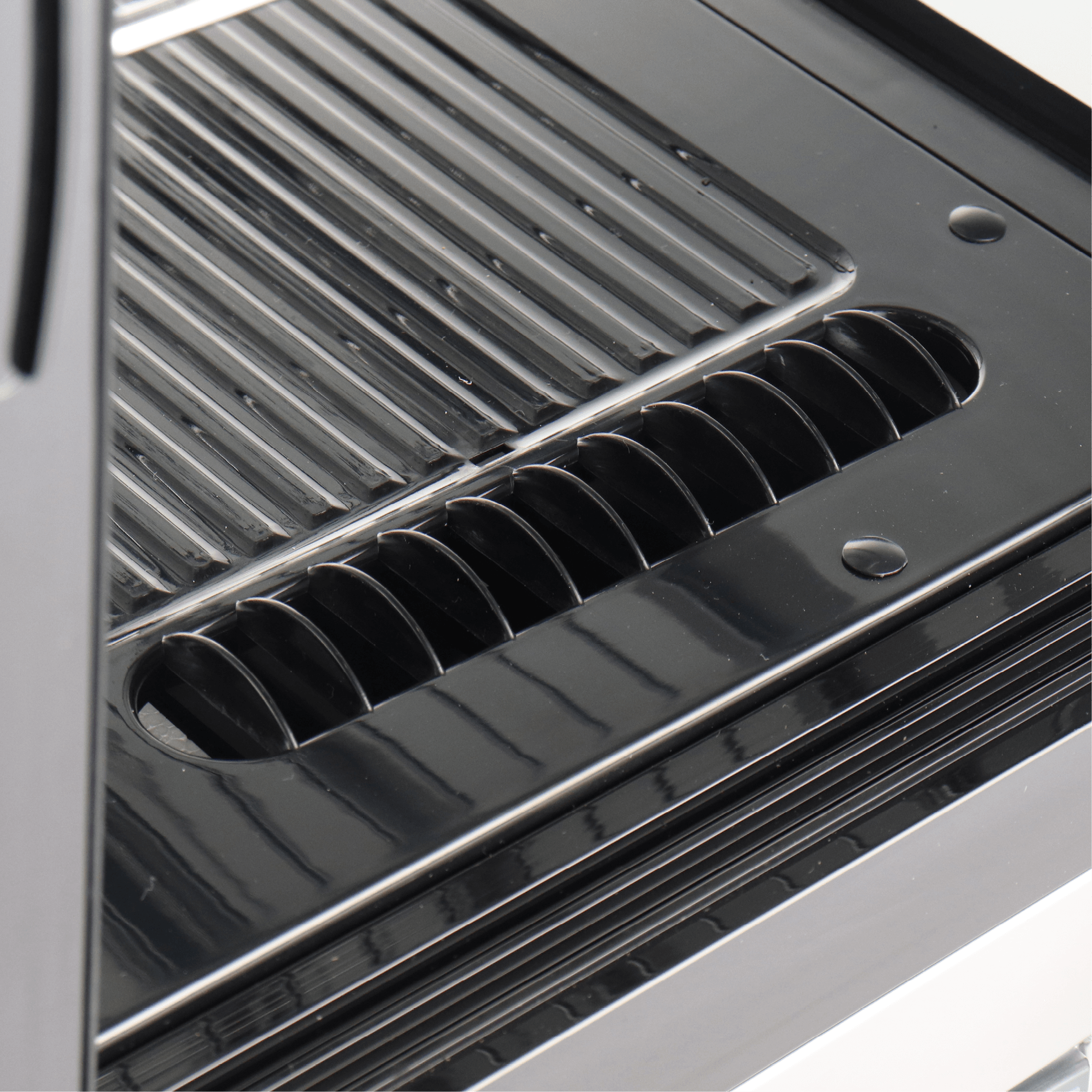 Close-up of black stainless steel interior with slotted ventilation and grooved shelving of curved cake display fridge.