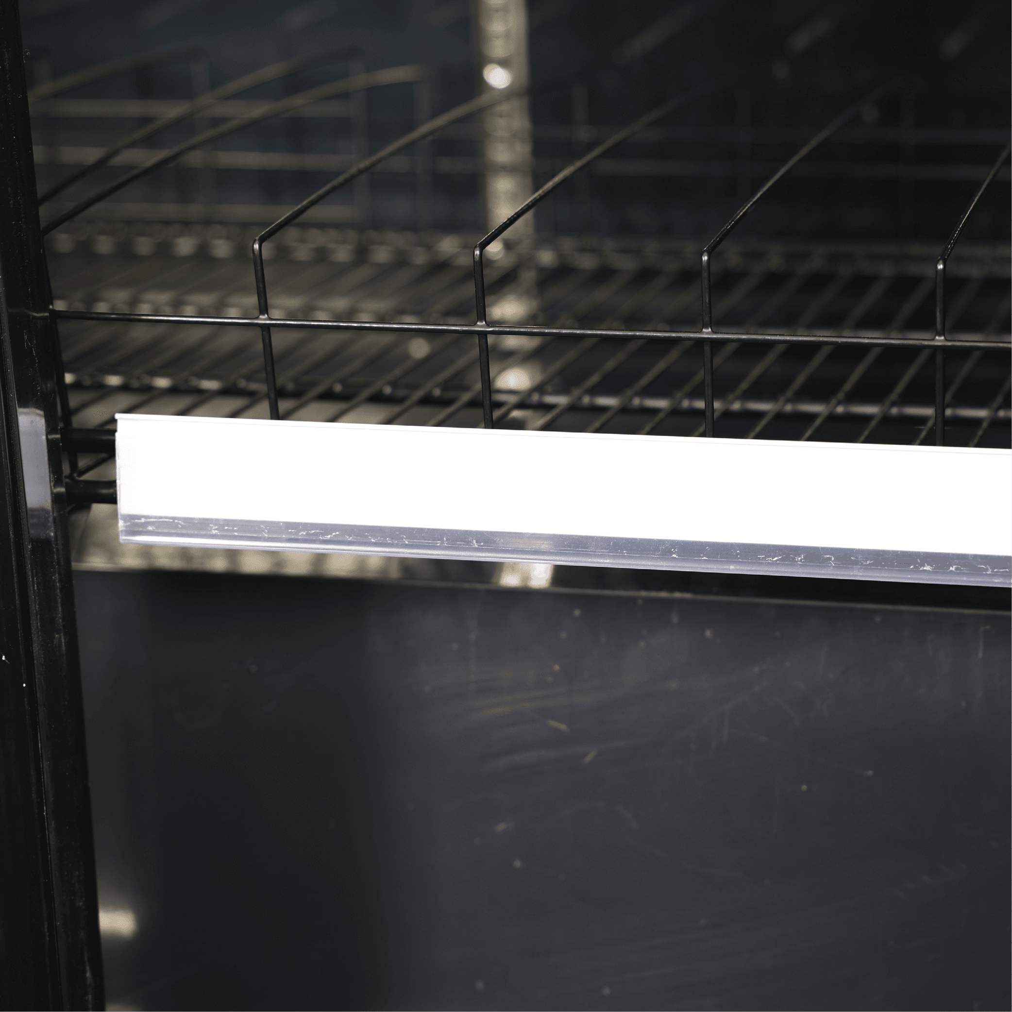 Black upright display fridge interior with metal wire shelving and bright LED light strip.