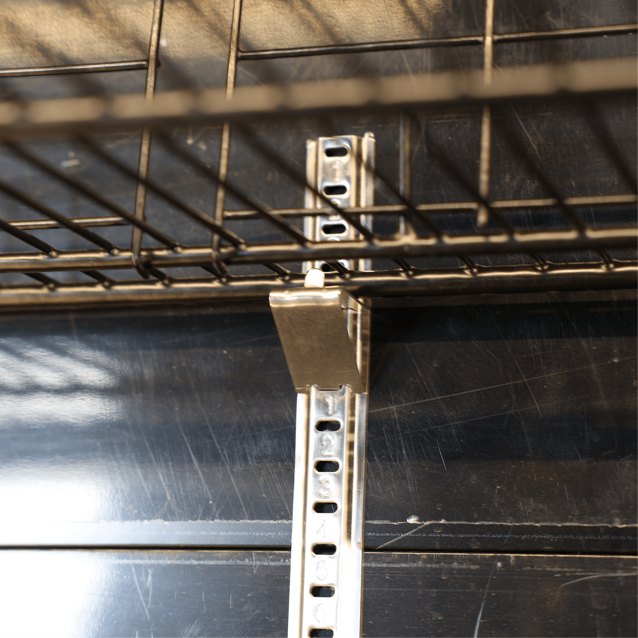Close-up view of adjustable metal shelving bracket and wire rack inside black upright glass door refrigerator.