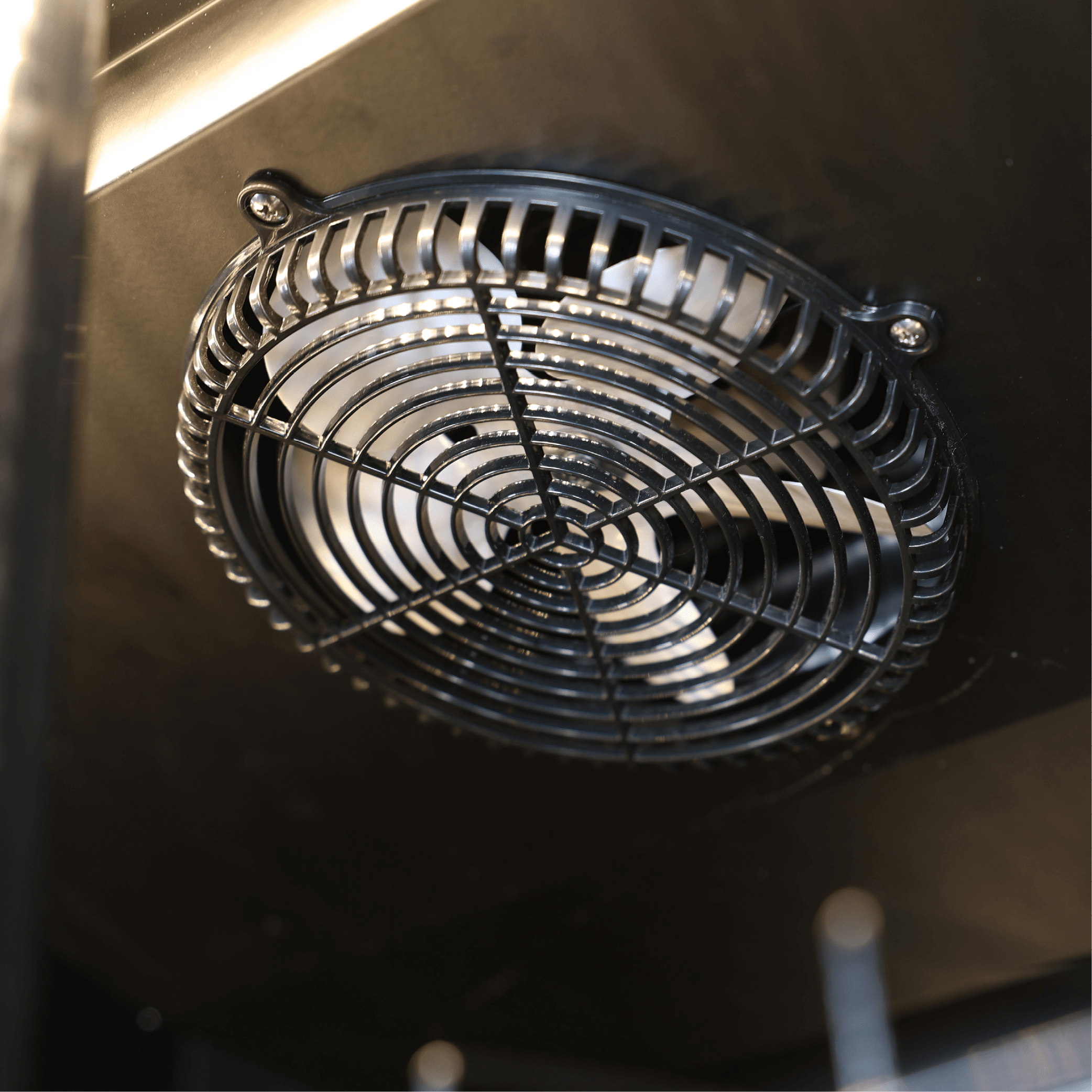Close-up of round black metal ventilation fan with protective grille inside refrigerator unit.