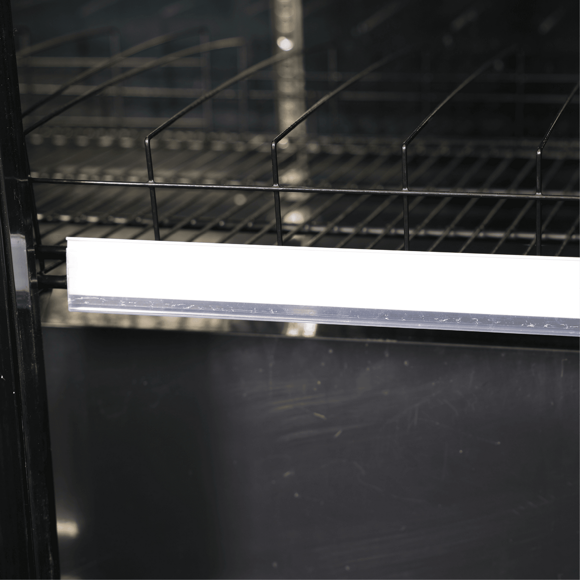 Close-up of black metal wire shelf with glossy black painted interior and LED light strip inside upright glass door fridge.