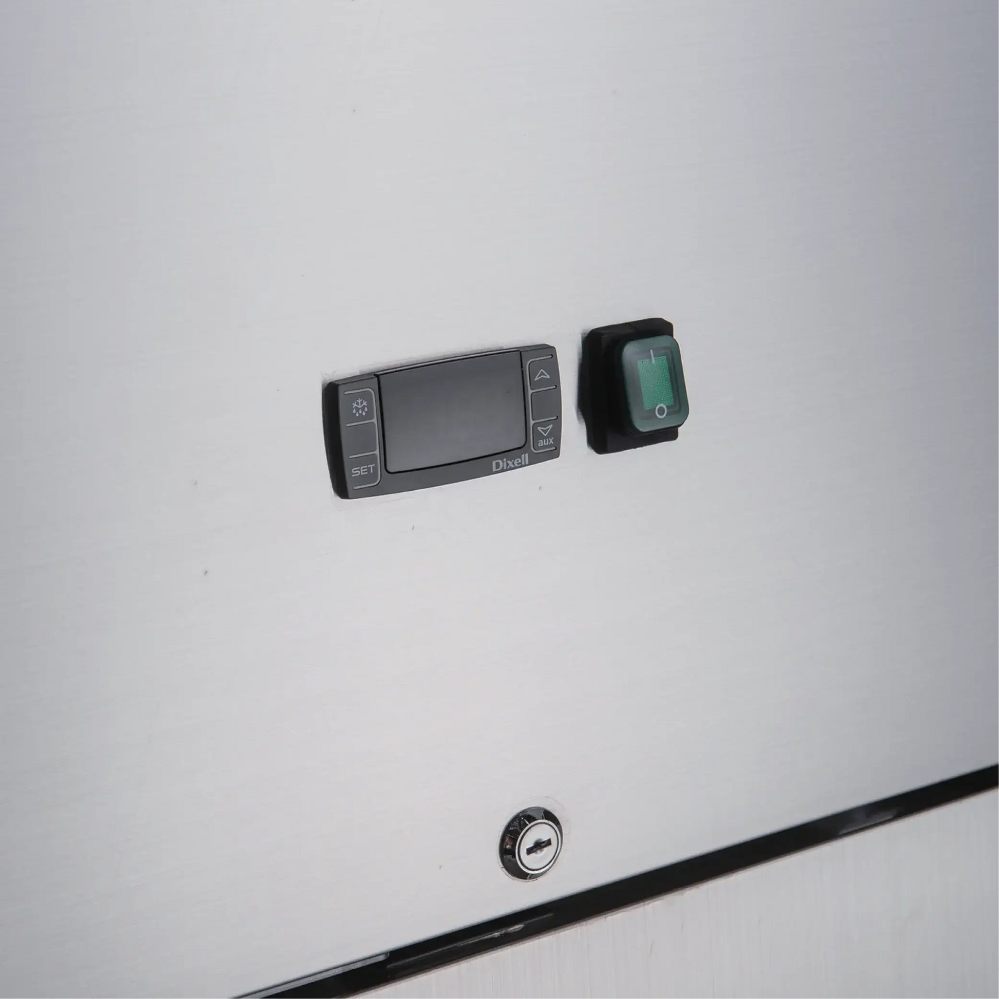Close-up of stainless steel refrigerator panel with digital control display, green power switch, and lock cylinder below.