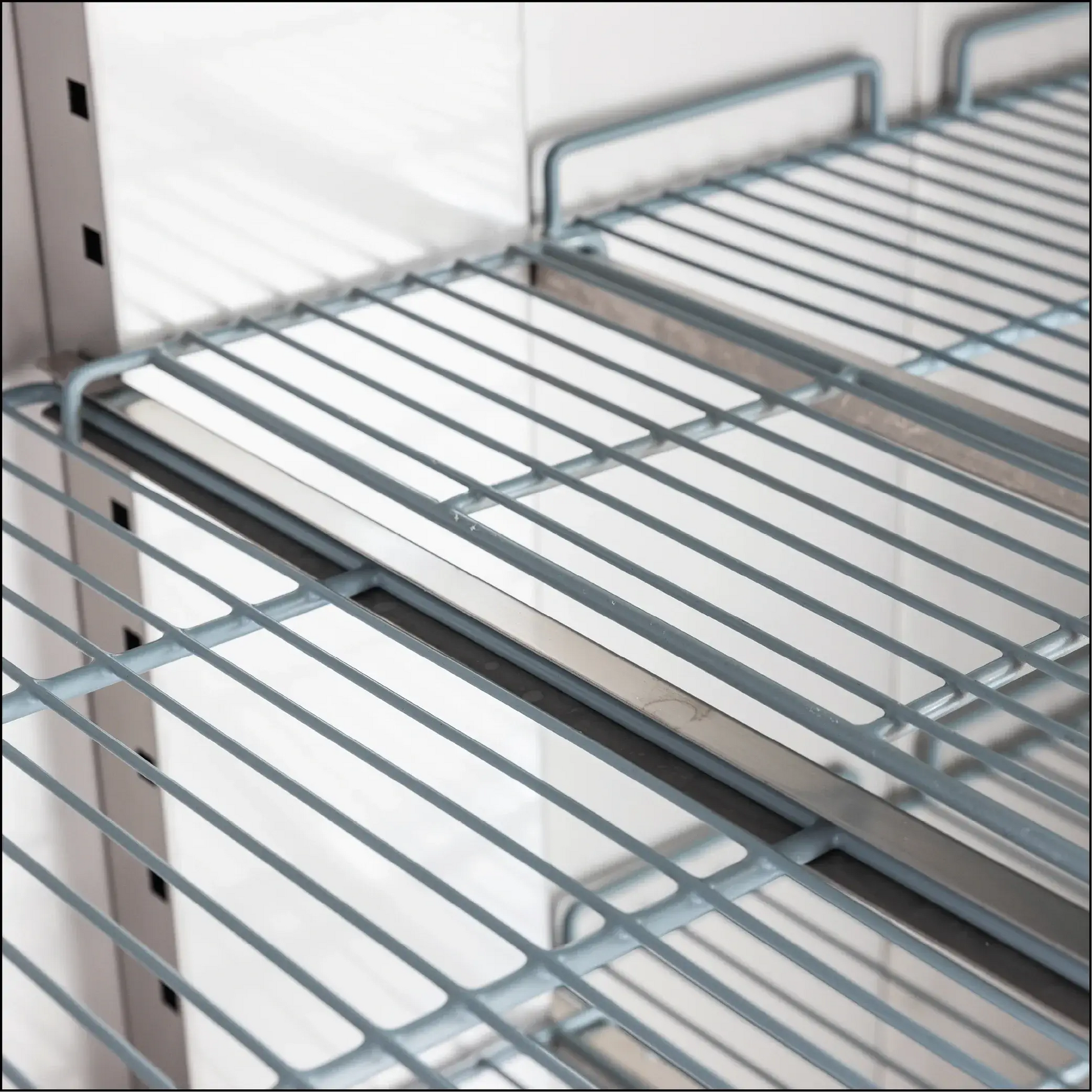 Close-up of silver metal wire shelves inside an upright stainless steel storage refrigerator.