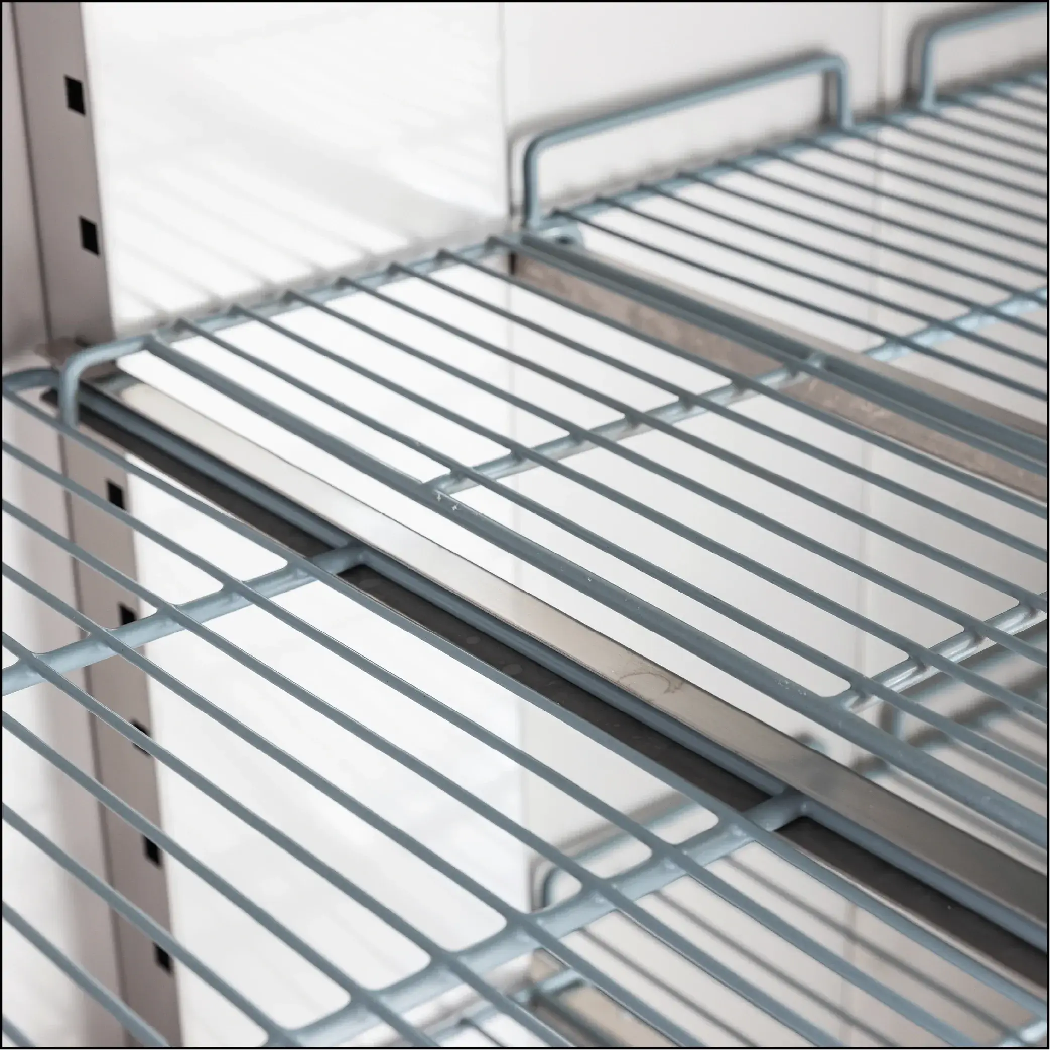 Close-up of silver metal wire shelves inside an upright stainless steel storage refrigerator.