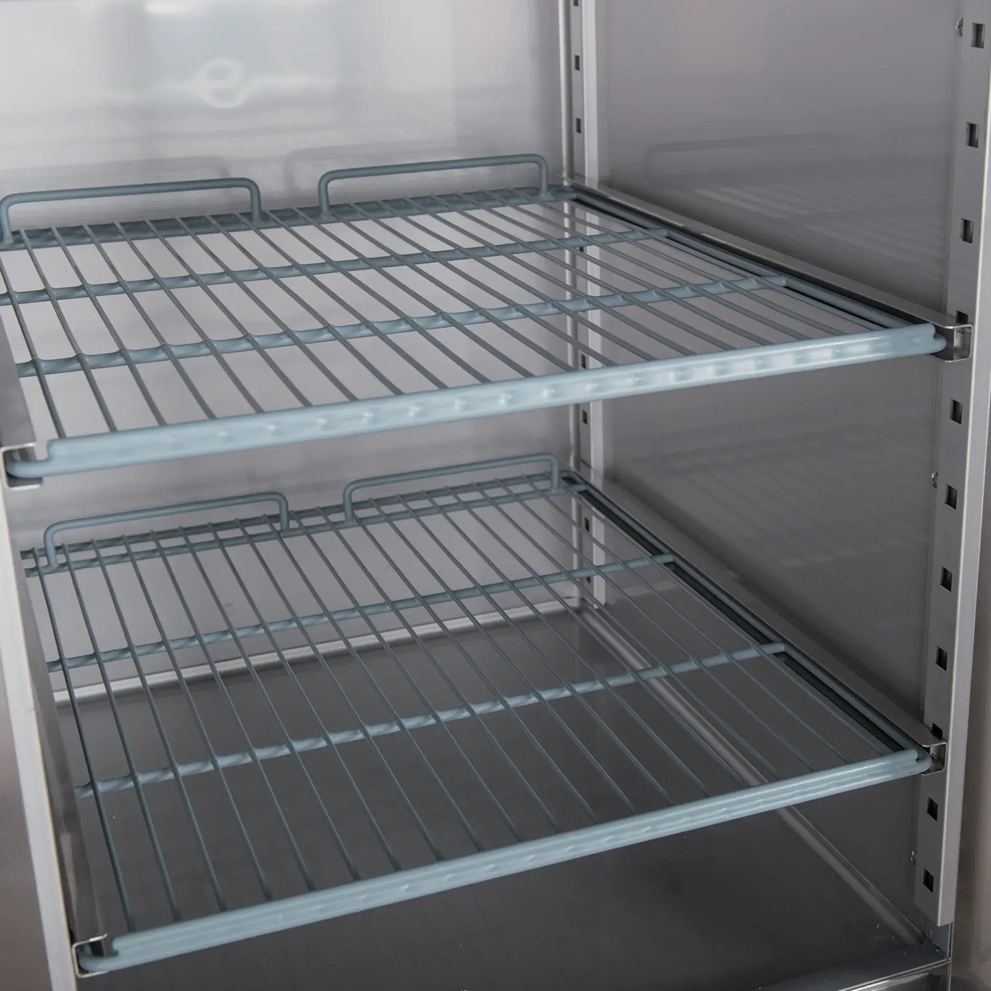 Interior view of stainless steel upright freezer with adjustable wire shelves and solid metal sides.