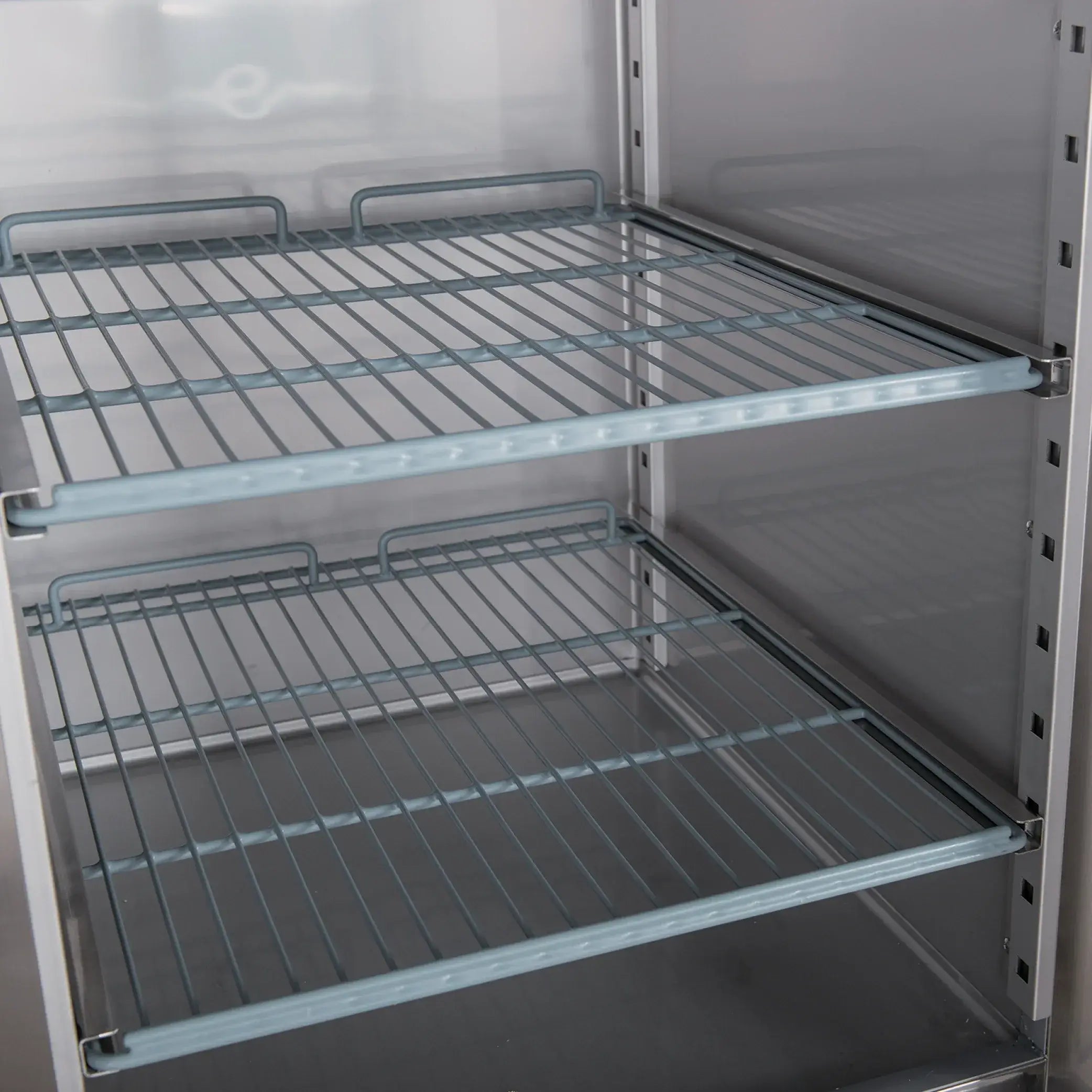 Interior view of stainless steel upright freezer with adjustable wire shelves and solid metal sides.