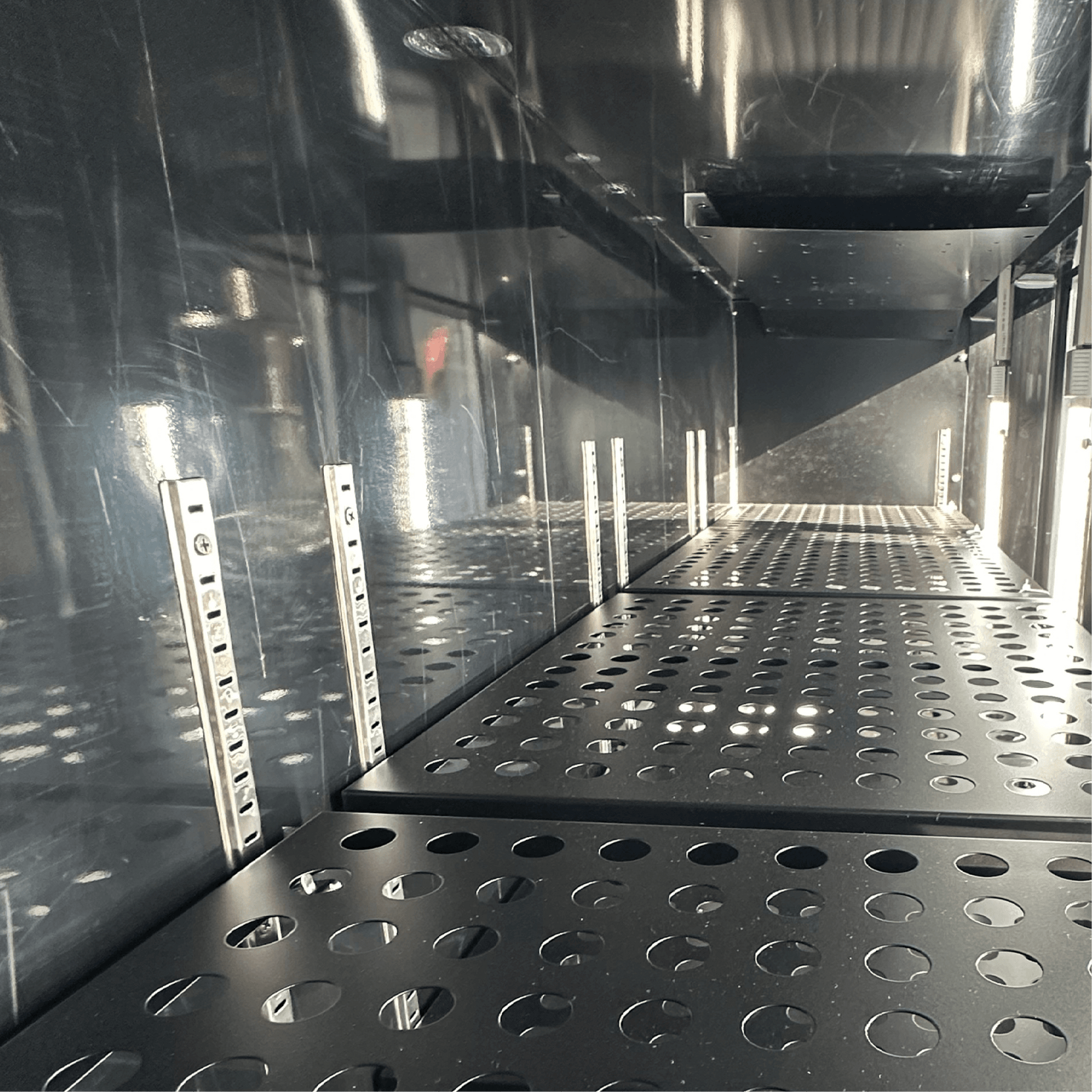 Interior view of stainless steel underbench refrigerator with adjustable perforated shelves and reflective surfaces.
