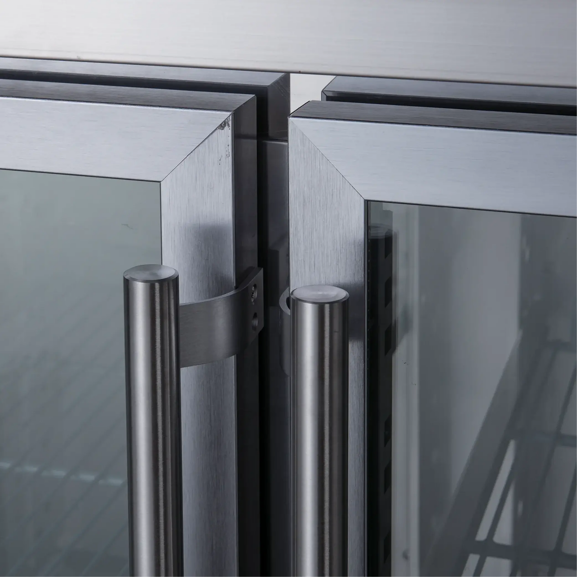 Close-up of stainless steel underbench refrigerator doors with vertical brushed metal handles and glass panels.