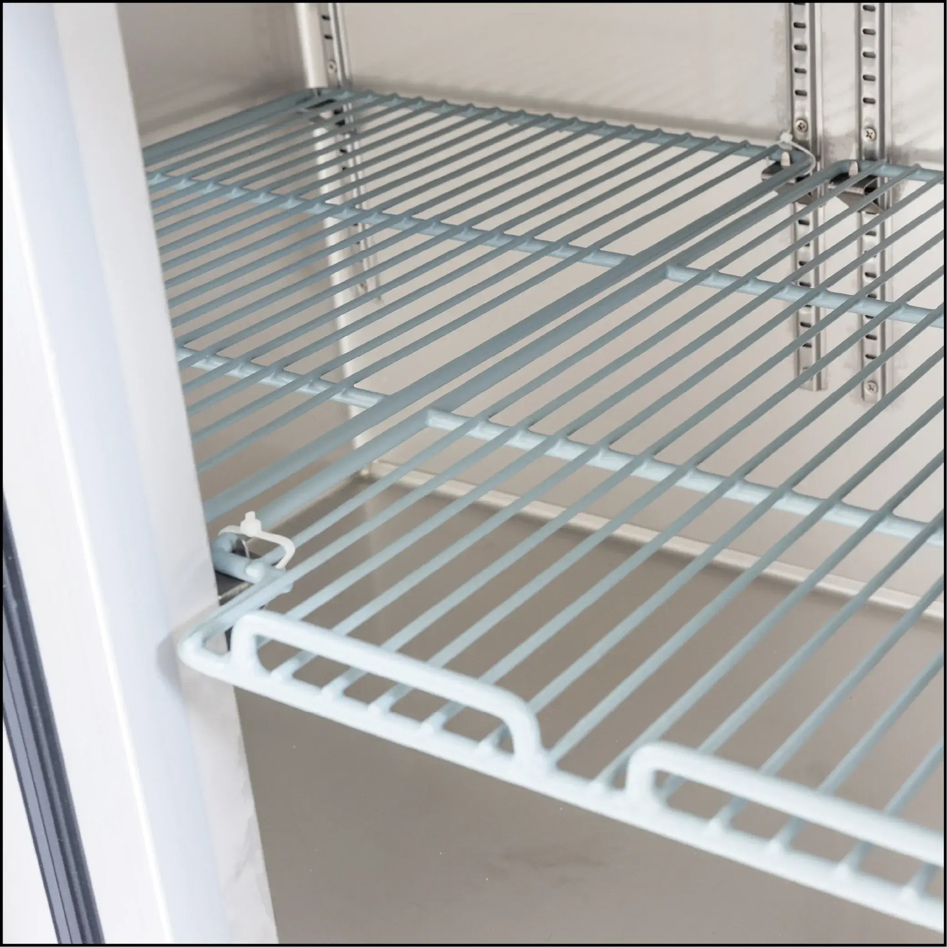 White metal wire shelf inside commercial underbench refrigerator with adjustable support brackets.