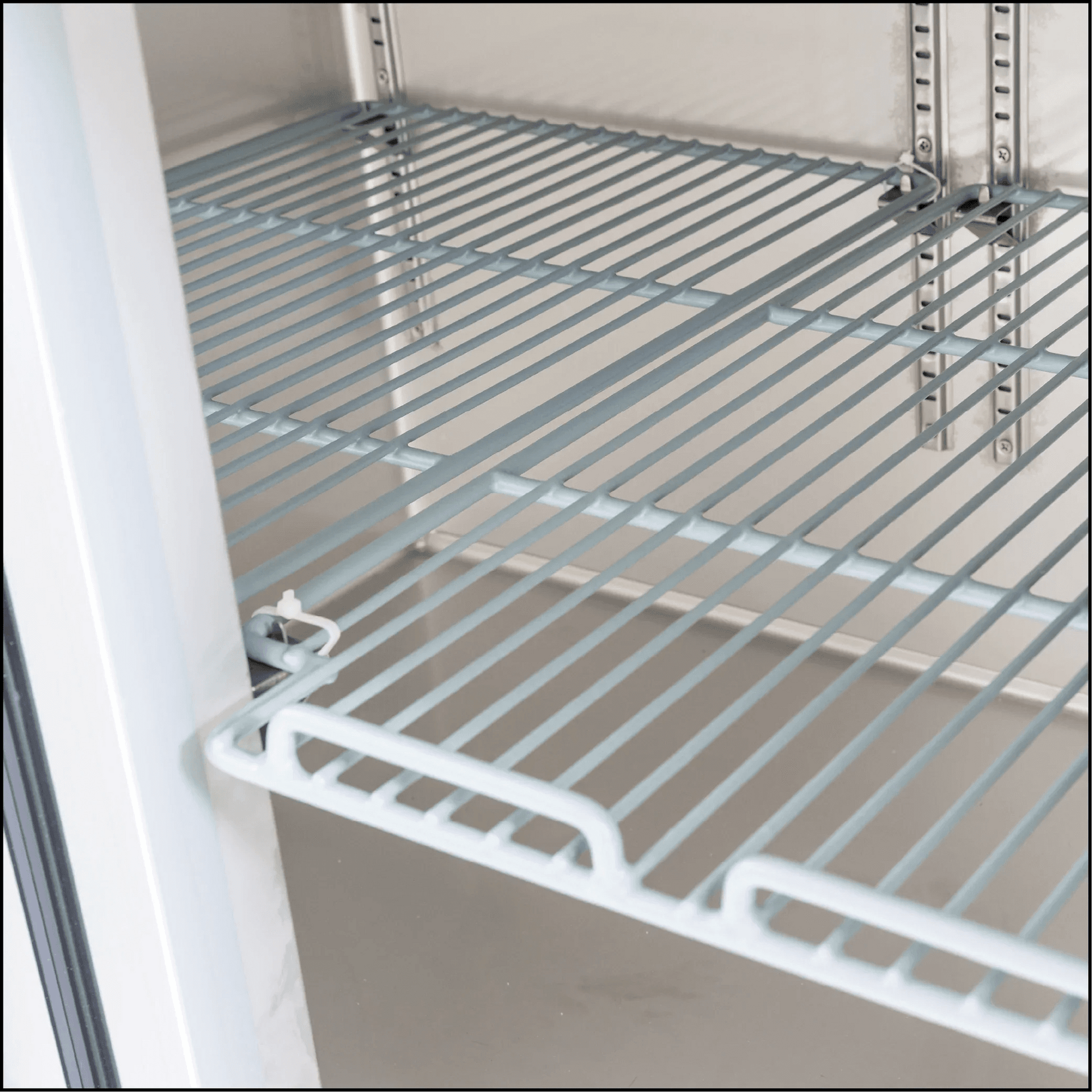 Stainless steel wire shelving inside underbench refrigerator with glass door frame visible.