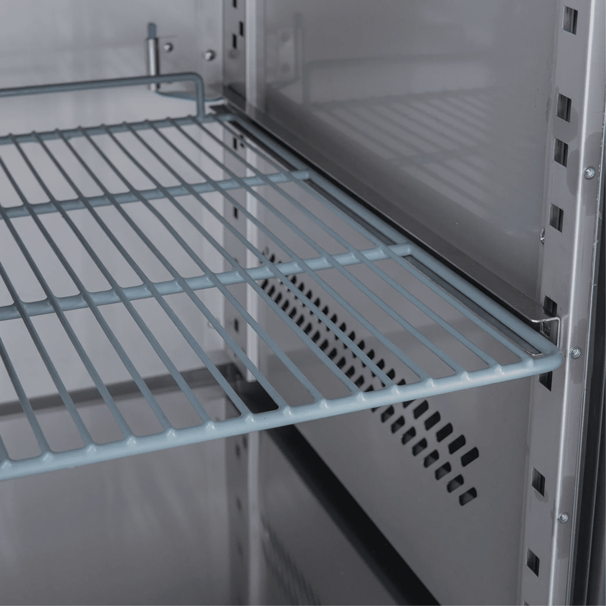 Interior view of stainless steel underbench refrigerator with adjustable wire shelving and ventilation panel.