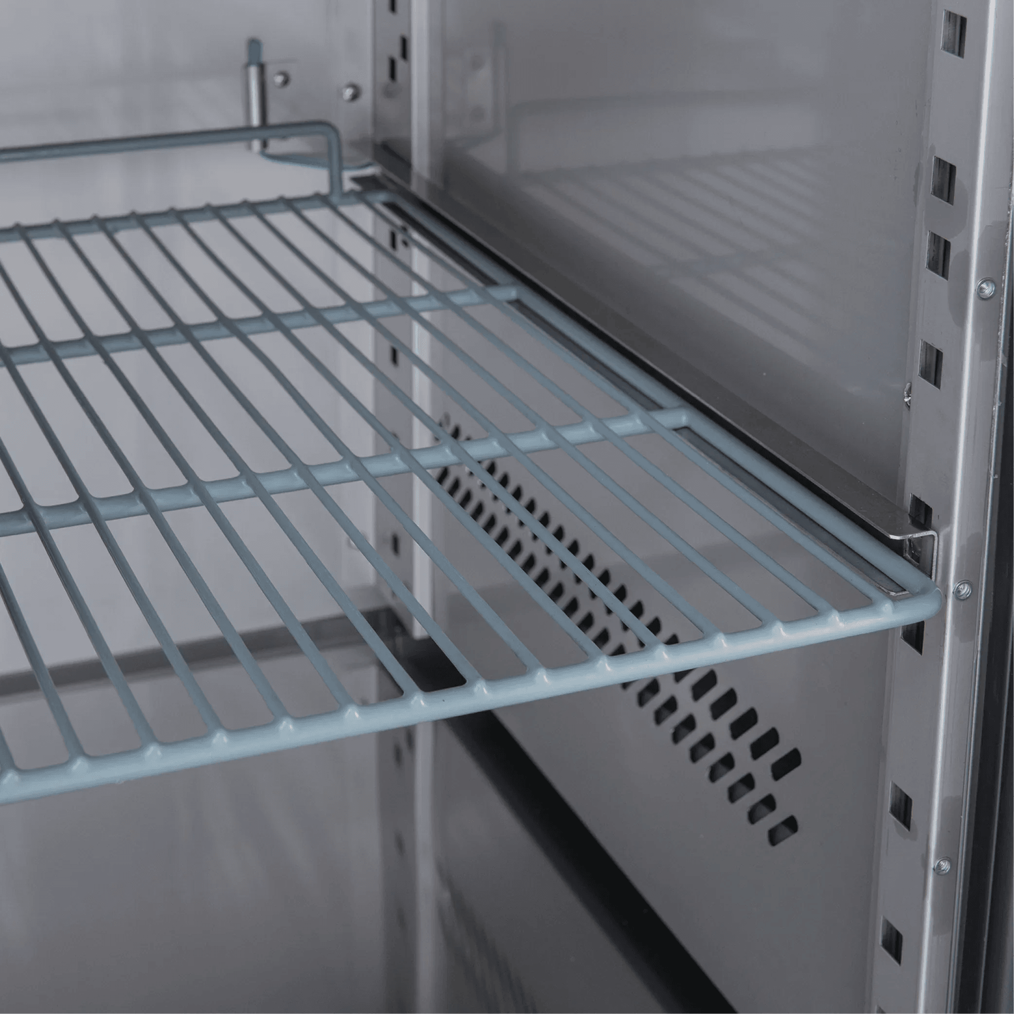 Interior view of stainless steel underbench refrigerator with adjustable wire shelving and ventilation panel.