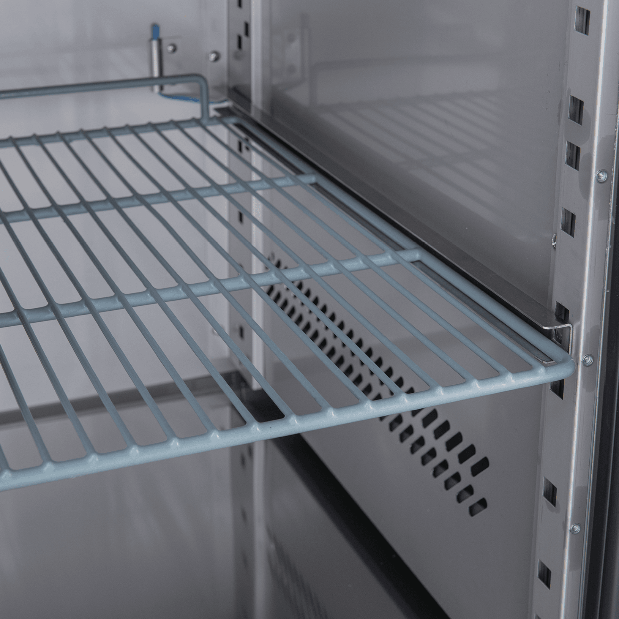Stainless steel underbench refrigerator interior with adjustable wire shelving and vented back panel.