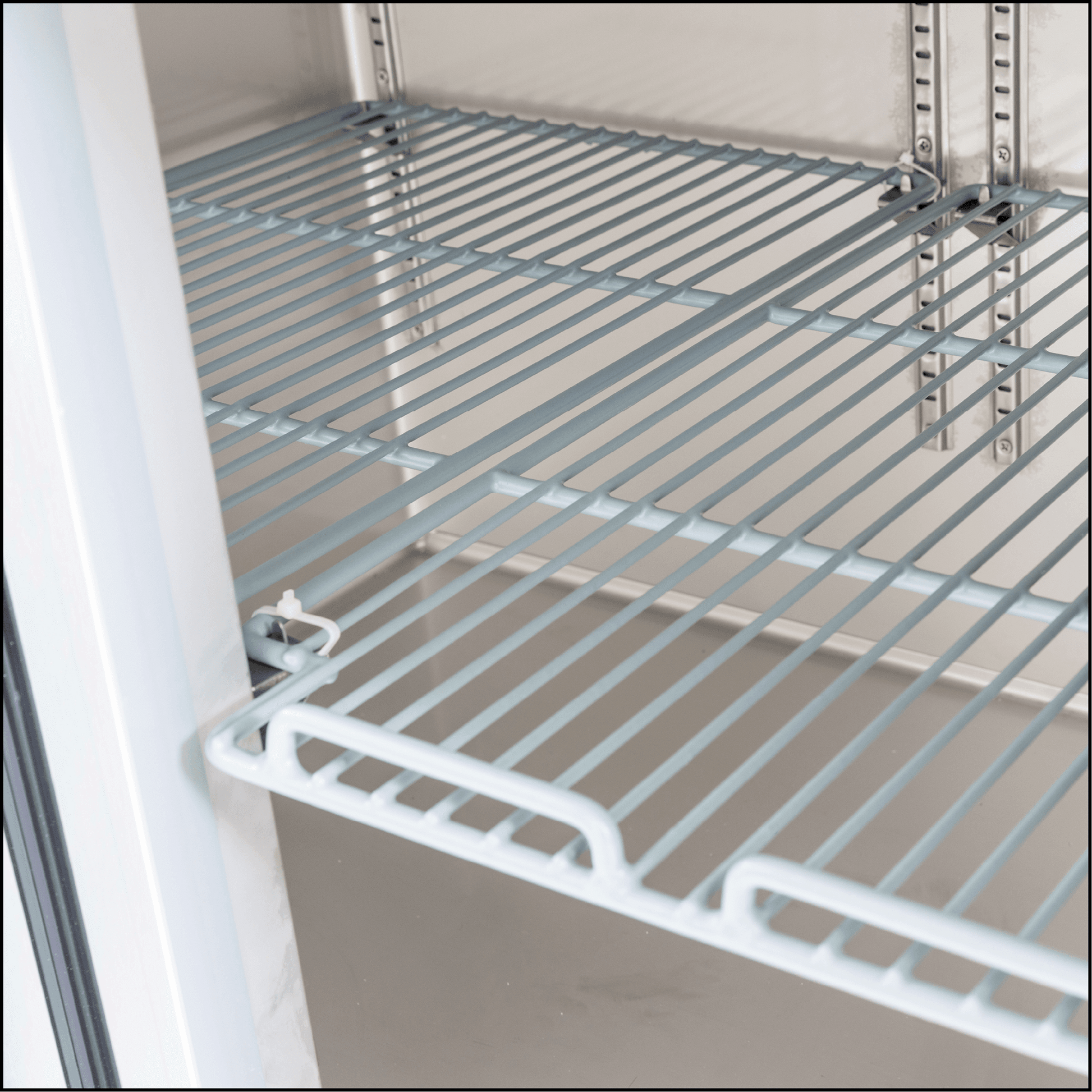 Stainless steel wire rack shelf inside commercial underbench refrigerator with glass doors.