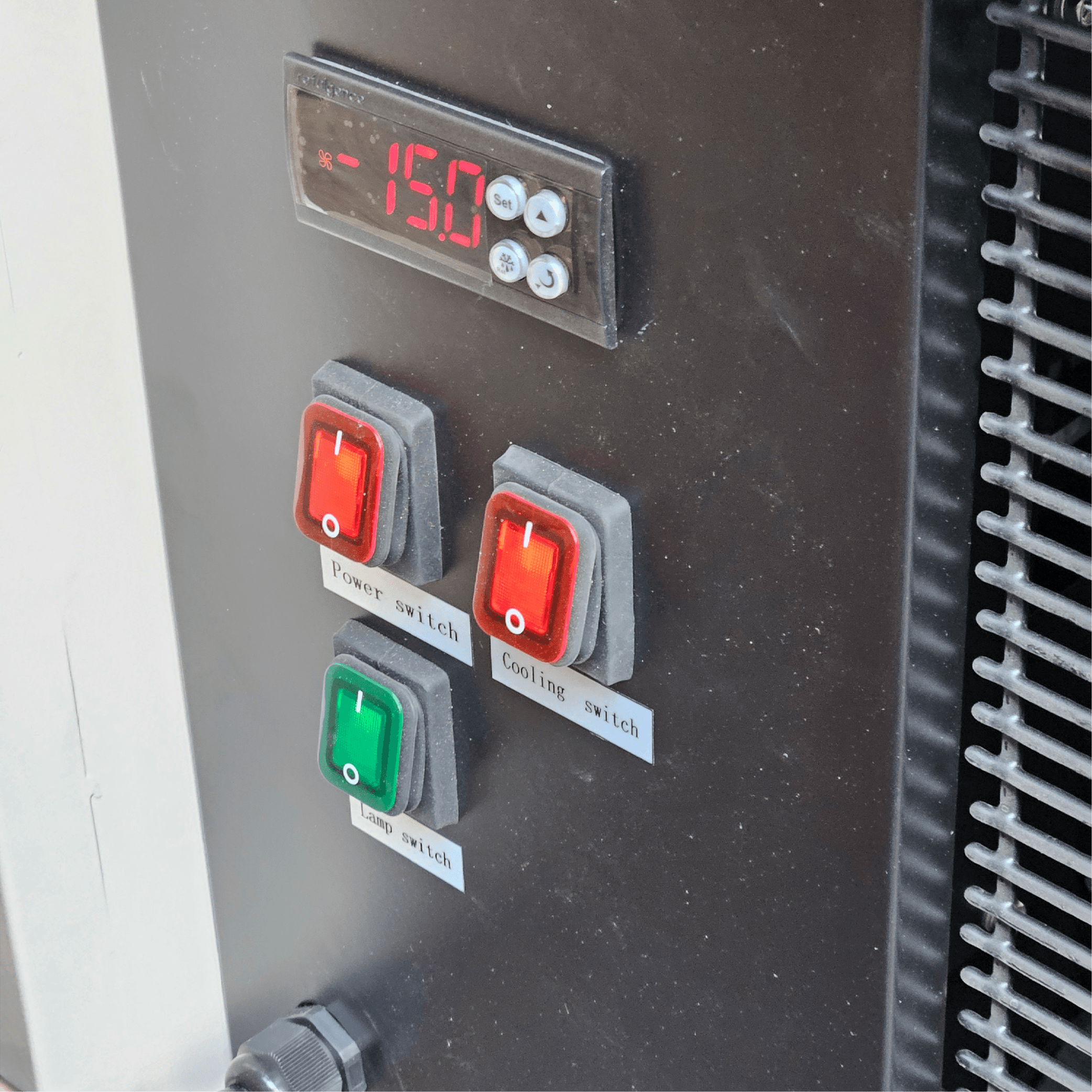 Control panel with digital temperature display and red and green power switches on black freezer surface.
