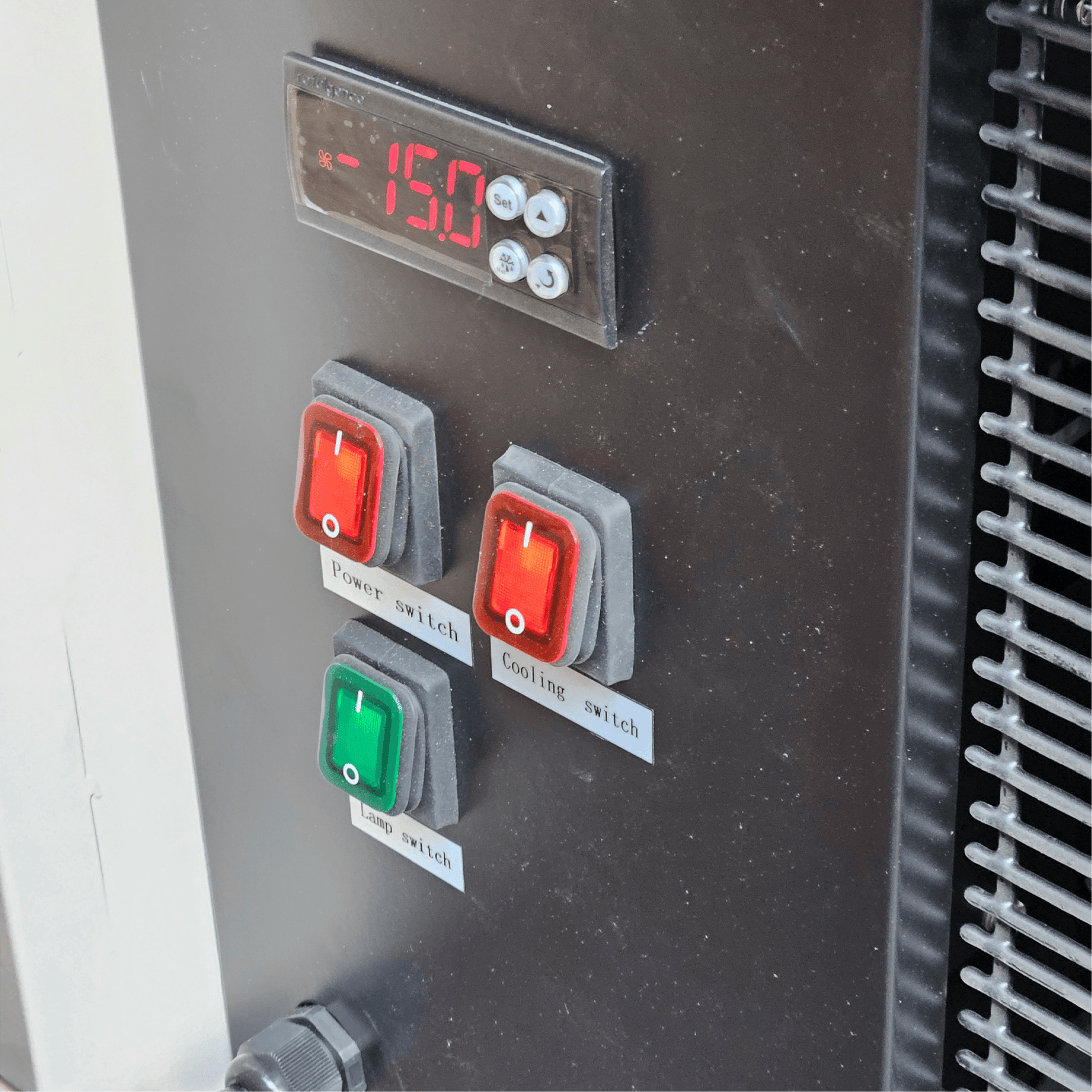 Black control panel with digital temperature display and three red and green toggle switches on a freezer unit.
