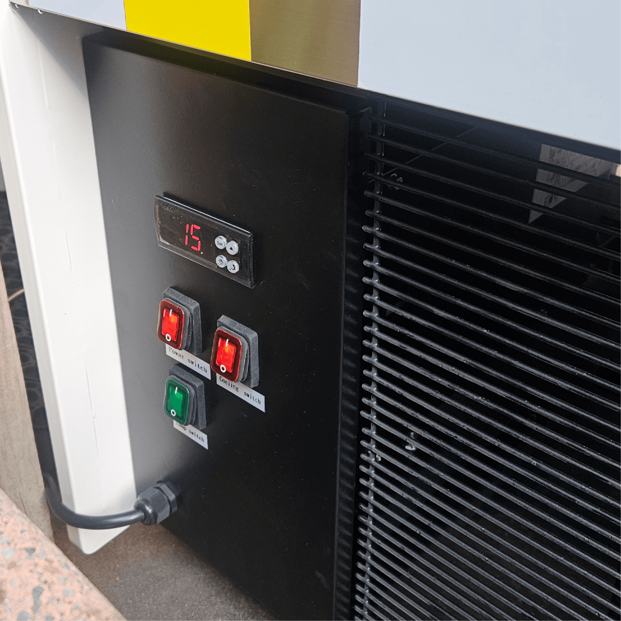 Black control panel with digital temperature display and three colored switches on white and black painted steel freezer.