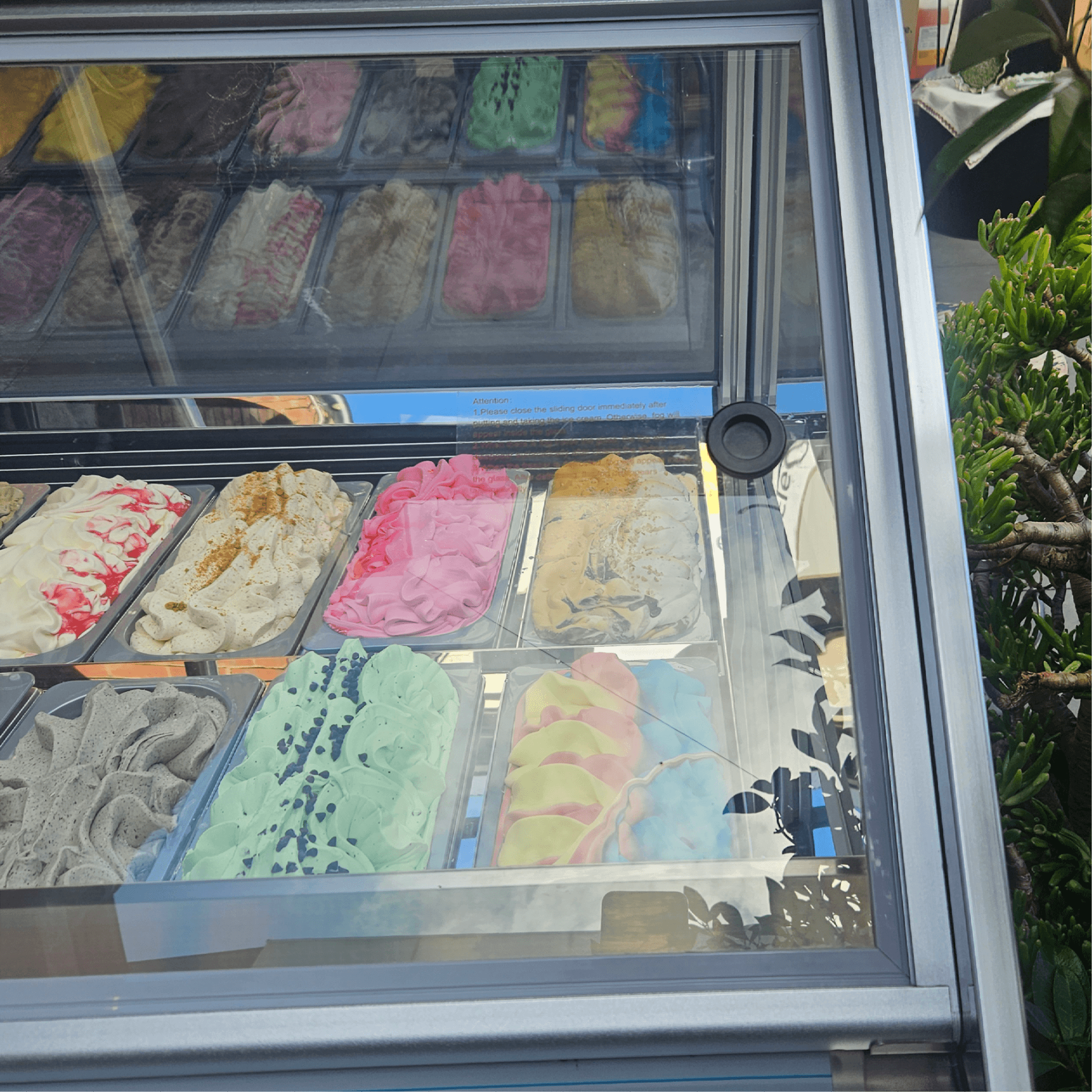 White steel and glass freezer with 18 colorful ice cream tubs arranged in three rows, angled glass display panel.