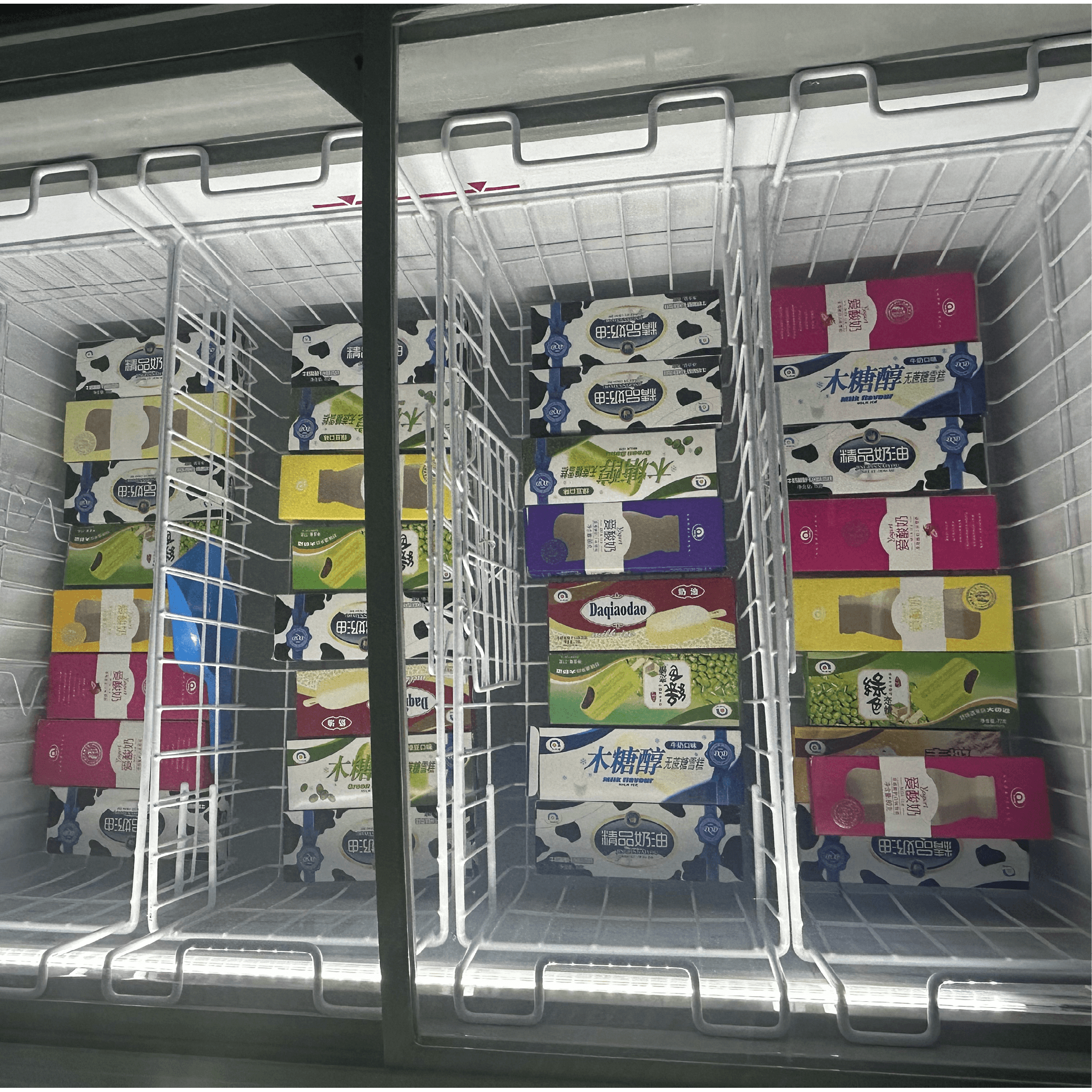 White curved glass chest freezer with LED lighting and four wire baskets filled with packaged frozen products.