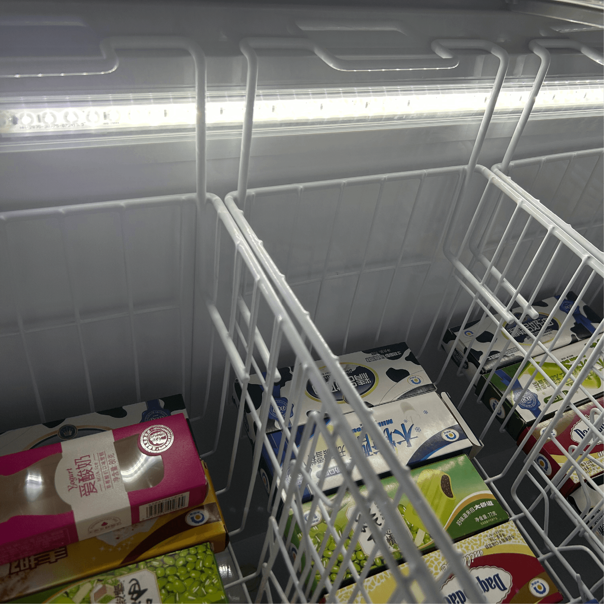 White flat glass display chest freezer with three wire baskets and internal LED lighting.