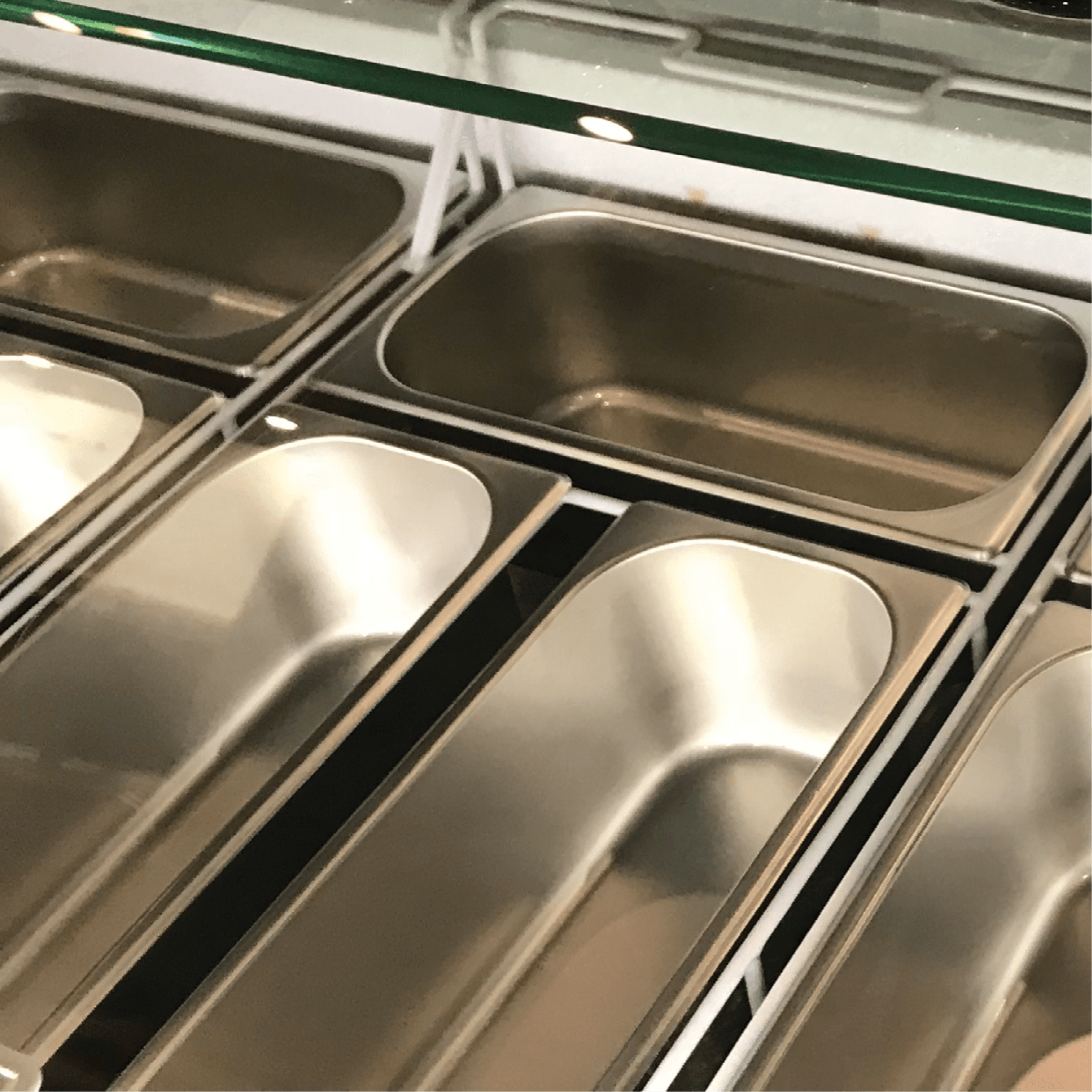 Commercial stainless steel ice cream freezer with twelve rectangular tubs and glass sneeze guard.