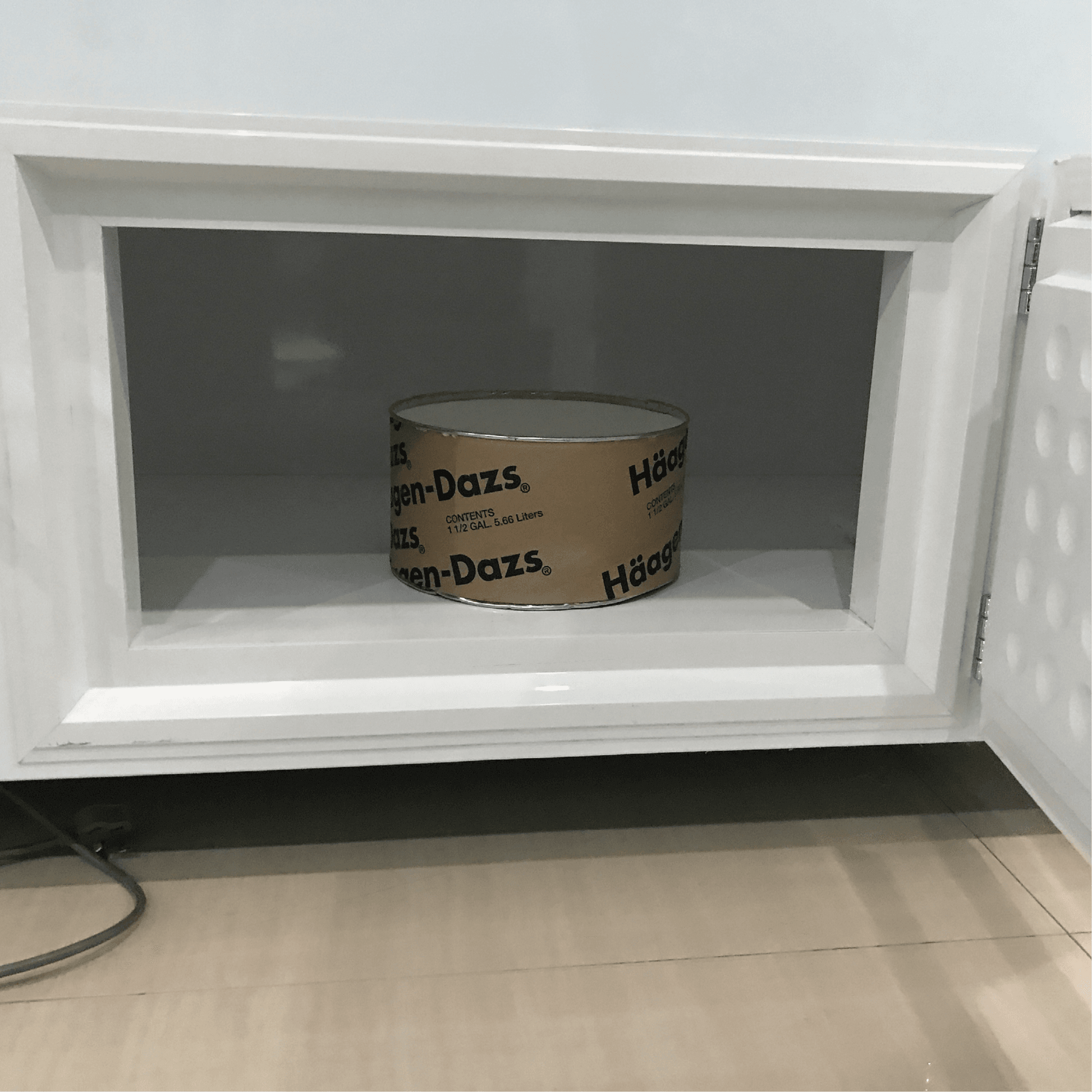 White painted steel freezer with glass door open, showing one Haagen-Dazs ice cream tub inside, bottom storage door visible.