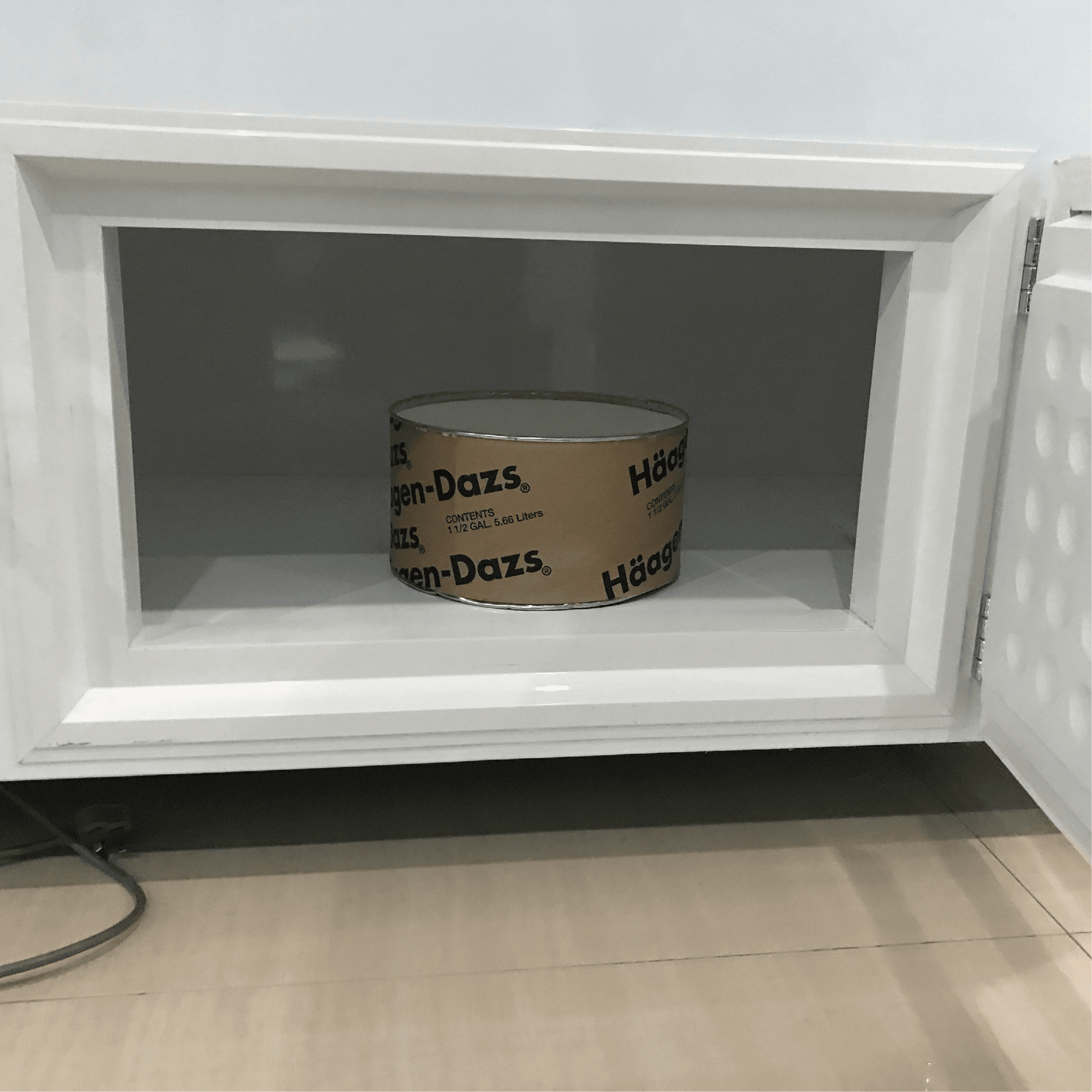 White painted steel freezer with glass door open, showing one Haagen-Dazs ice cream tub inside, bottom storage door visible.