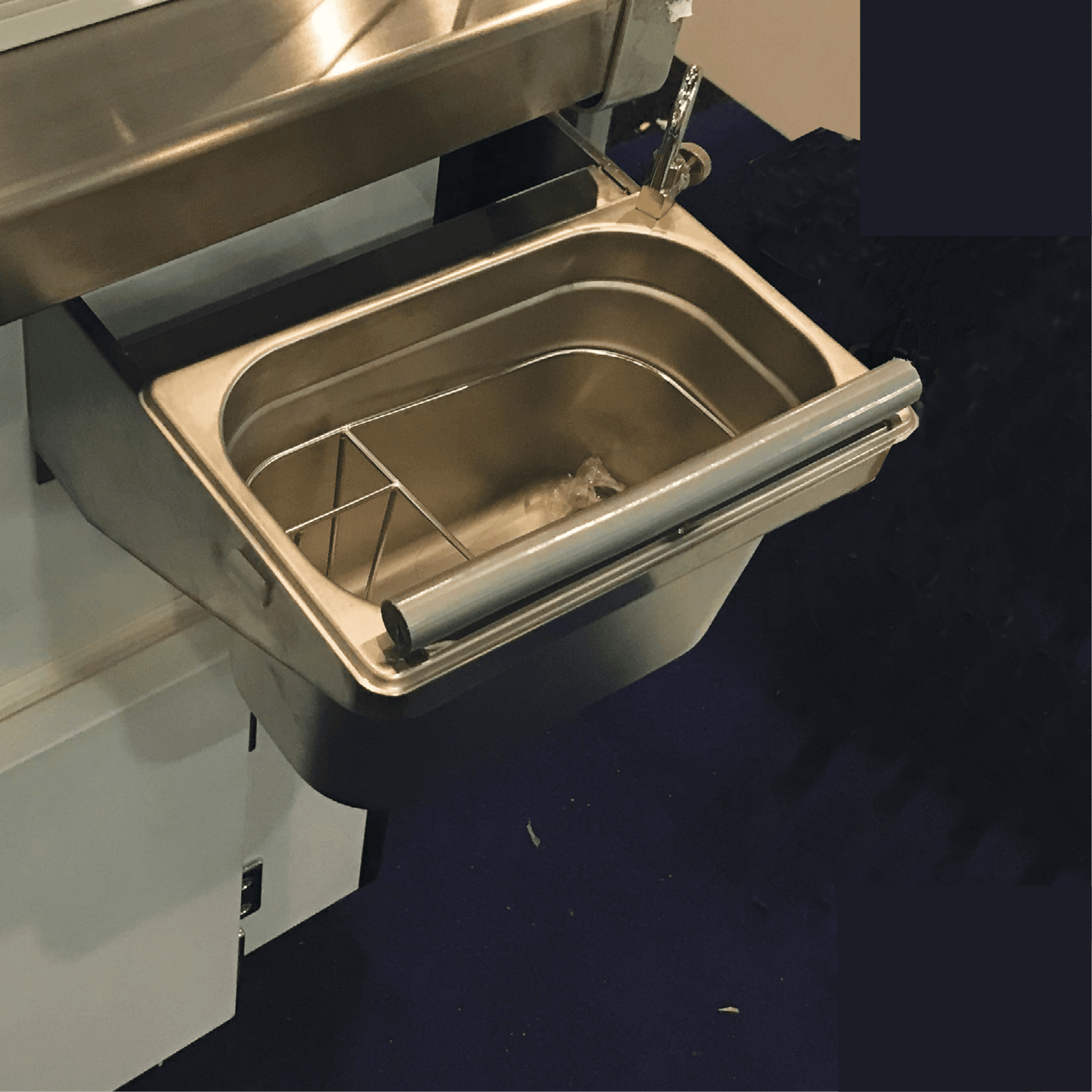 Stainless steel rectangular scoop washer with rounded corners and a sturdy handle attached to a white panel freezer unit.